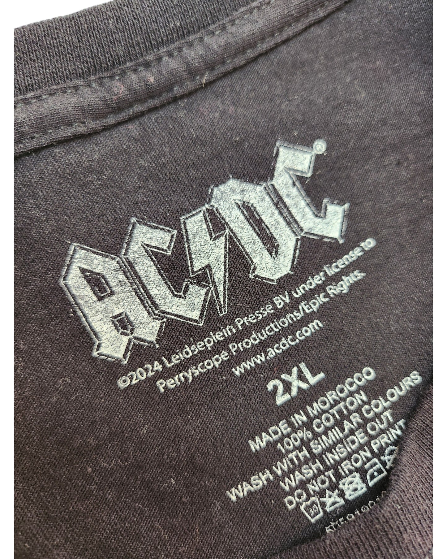Close-up of a black AC/DC upcycled breastfeeding & pumping leopard band t-shirt, size 2XL, featuring the logo, copyright info, and care instructions. Made in Morocco from 100% cotton. Preloved fashion item.