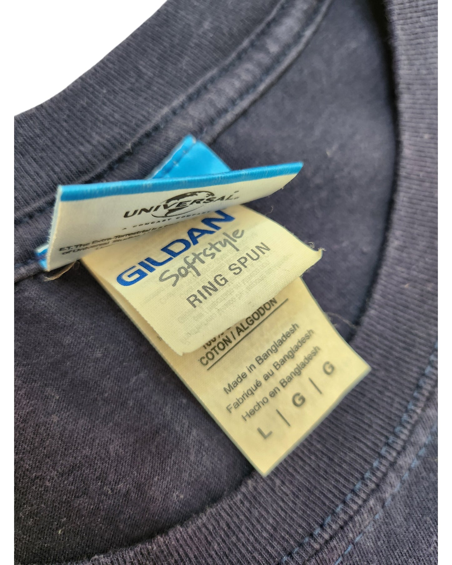 Close-up of a navy blue Upcycled Breastfeeding (Nursing) & Pumping ET t-shirt in size L by Gildan, showing the collar with two tags—main tag notes Gildan branding, size info, and eco-friendly, upcycled material; made in Bangladesh.