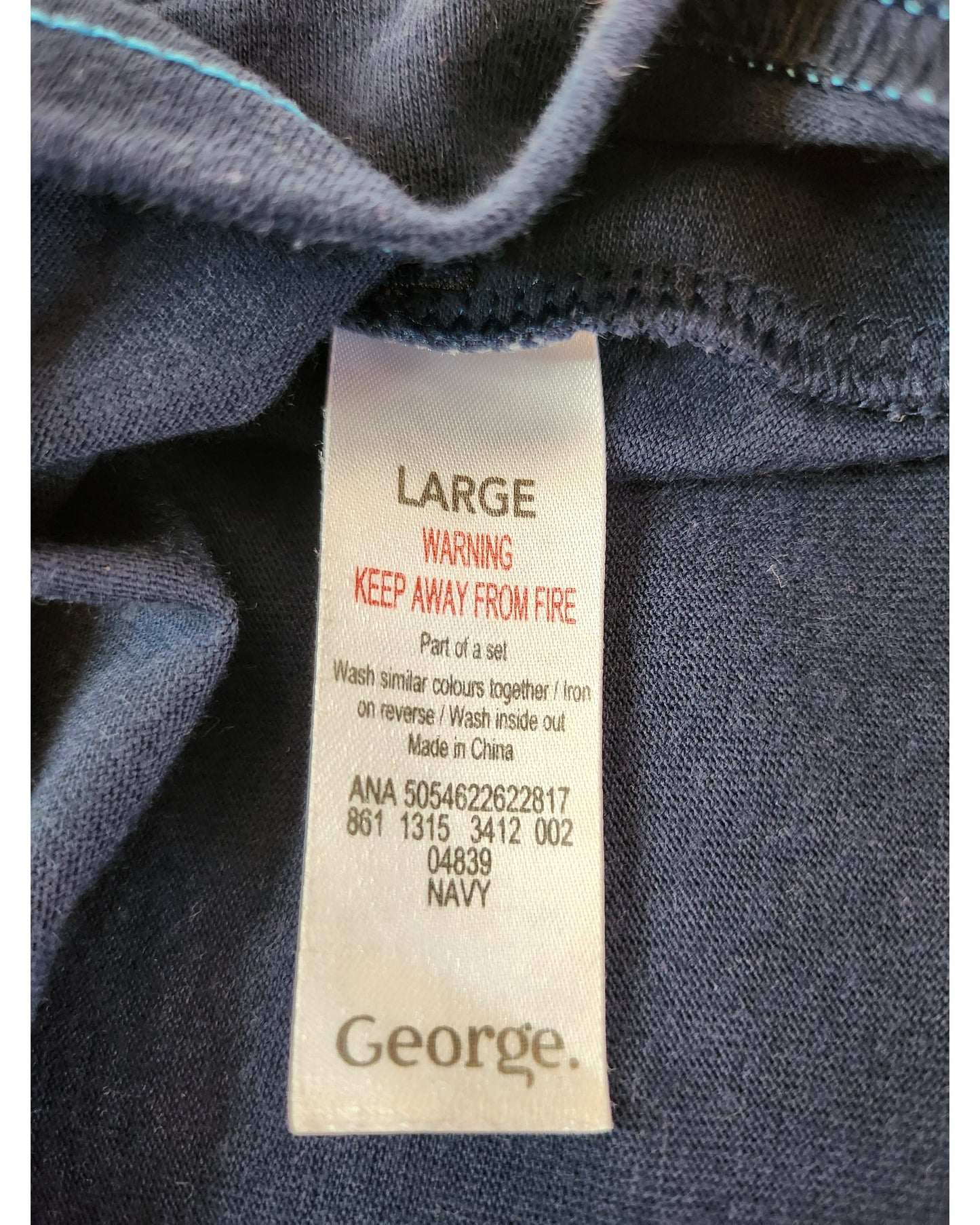 A close-up of the label on a navy Upcycled Breastfeeding & Pumping Cookie Monster t-shirt L by George shows size, fire warning, care details, product code, and the George brand—ideal for eco-conscious nursing moms.