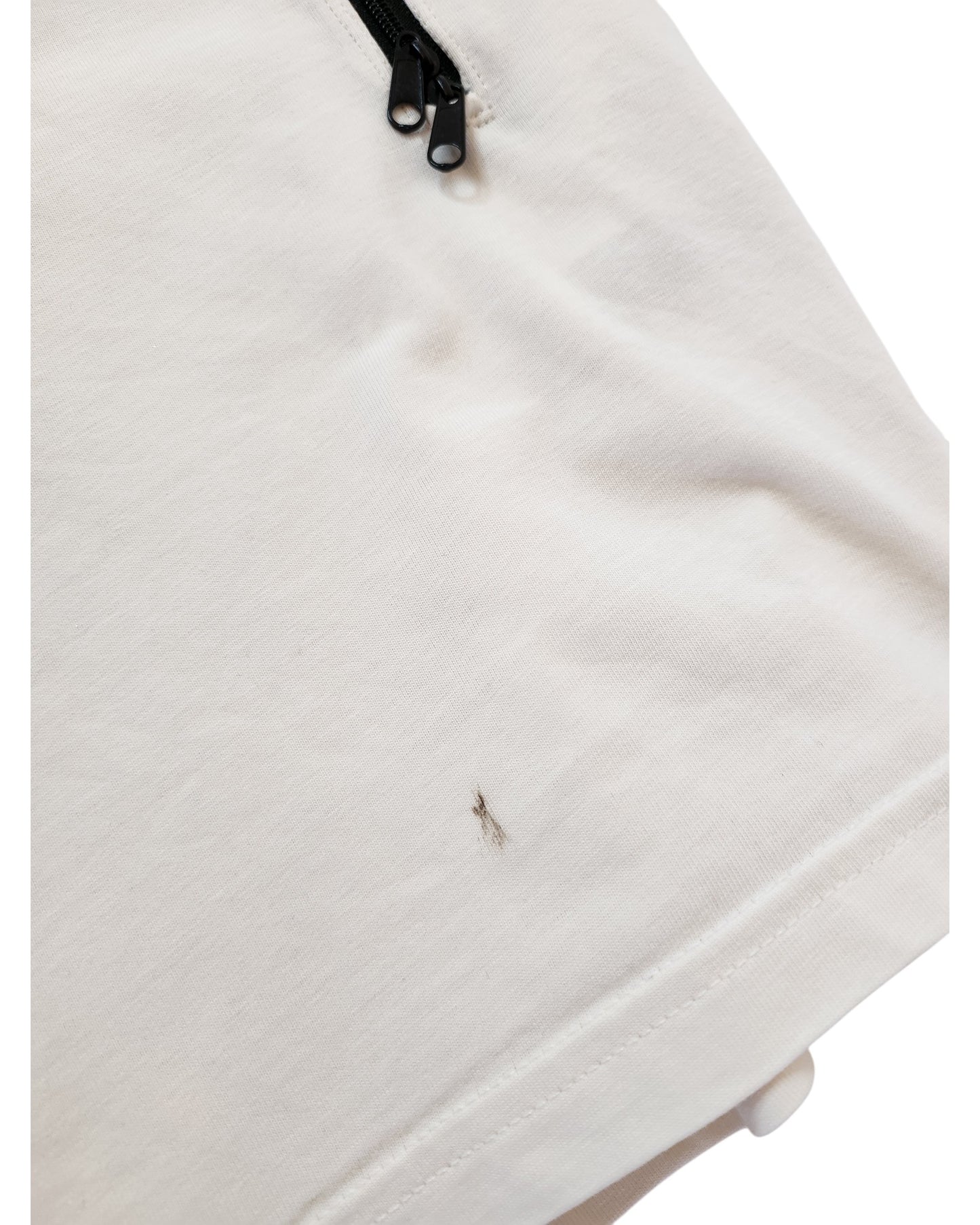 A close-up of a white H&M Upcycled Breastfeeding & Pumping The Rolling Stones t-shirt (XL, cream/red) shows a small thin black stain near the bottom hem and a black zipper at the top.
