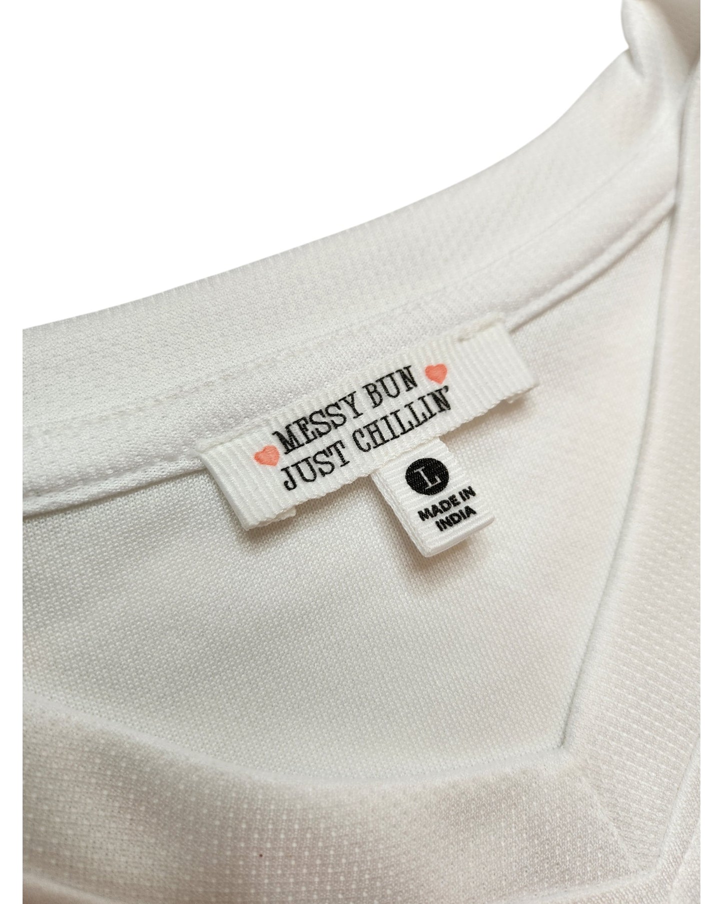 Close-up of a white Upcycled Breastfeeding & Pumping 89 Swiftie Football Jersey t-shirt (L) from Messy Bun Just Chillin, showing two tags—one with brand and pink hearts, and one labeled L MADE IN INDIA. A fresh take on preloved fashion.