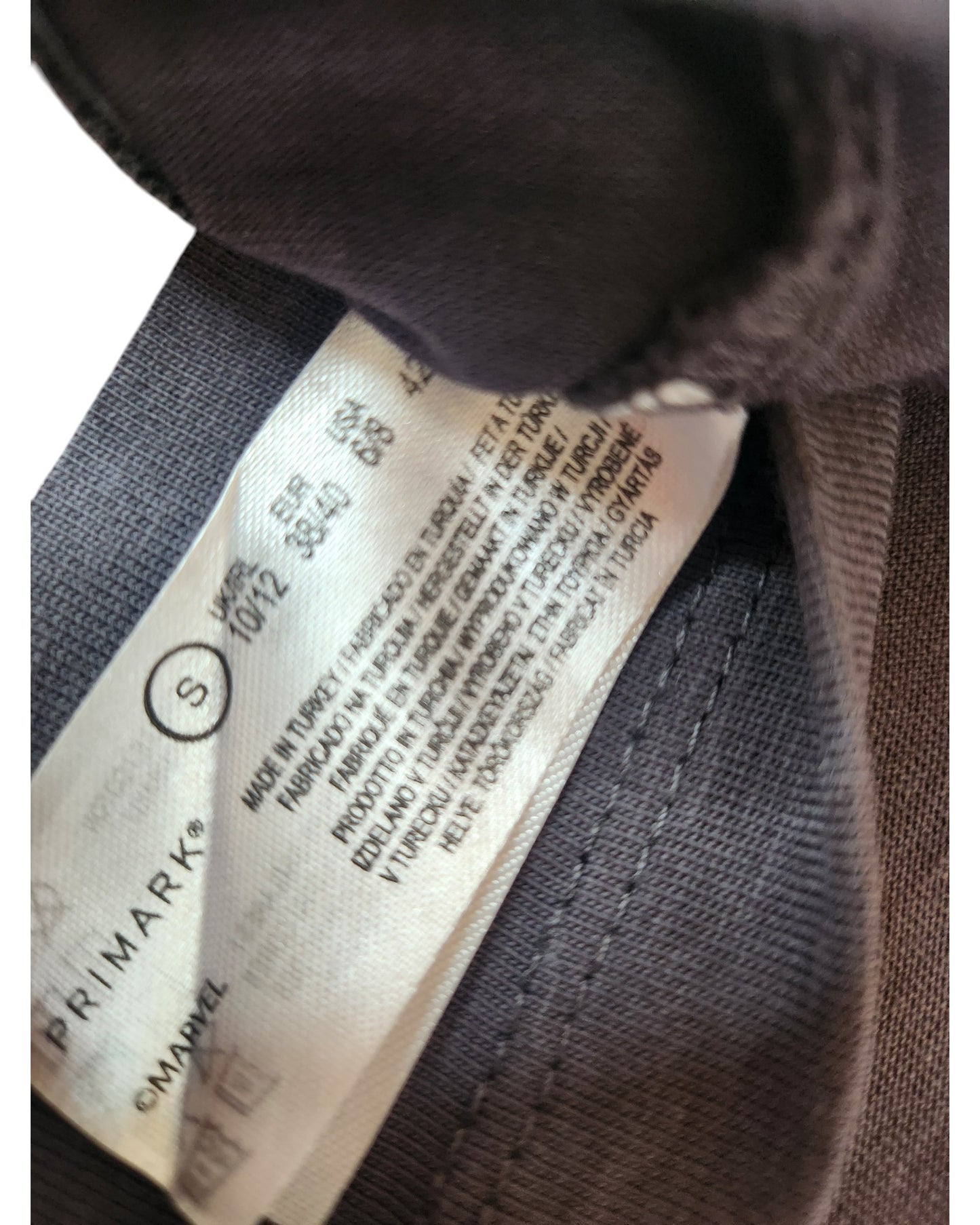 A close-up of a label inside a dark, affordable Primark Upcycled Breastfeeding & Pumping Hulk Marvel t-shirt (size S, UK10/12), showing washing instructions and multilingual text alongside the Marvel logo.