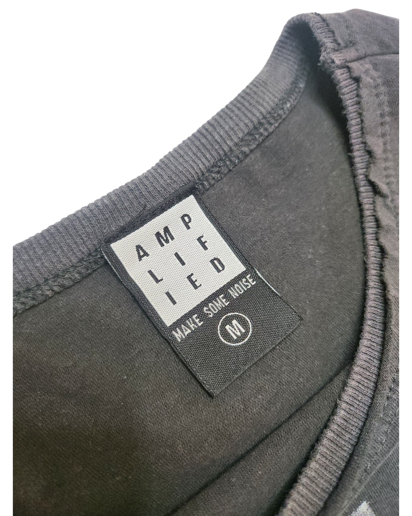 Close-up of a black Amplified label on an upcycled Metallica Guitar Band breastfeeding & pumping t-shirt (M), reading AMPLIFIED and MAKE SOME NOISE with a circled M for medium. The eco-friendly neckline is also shown.