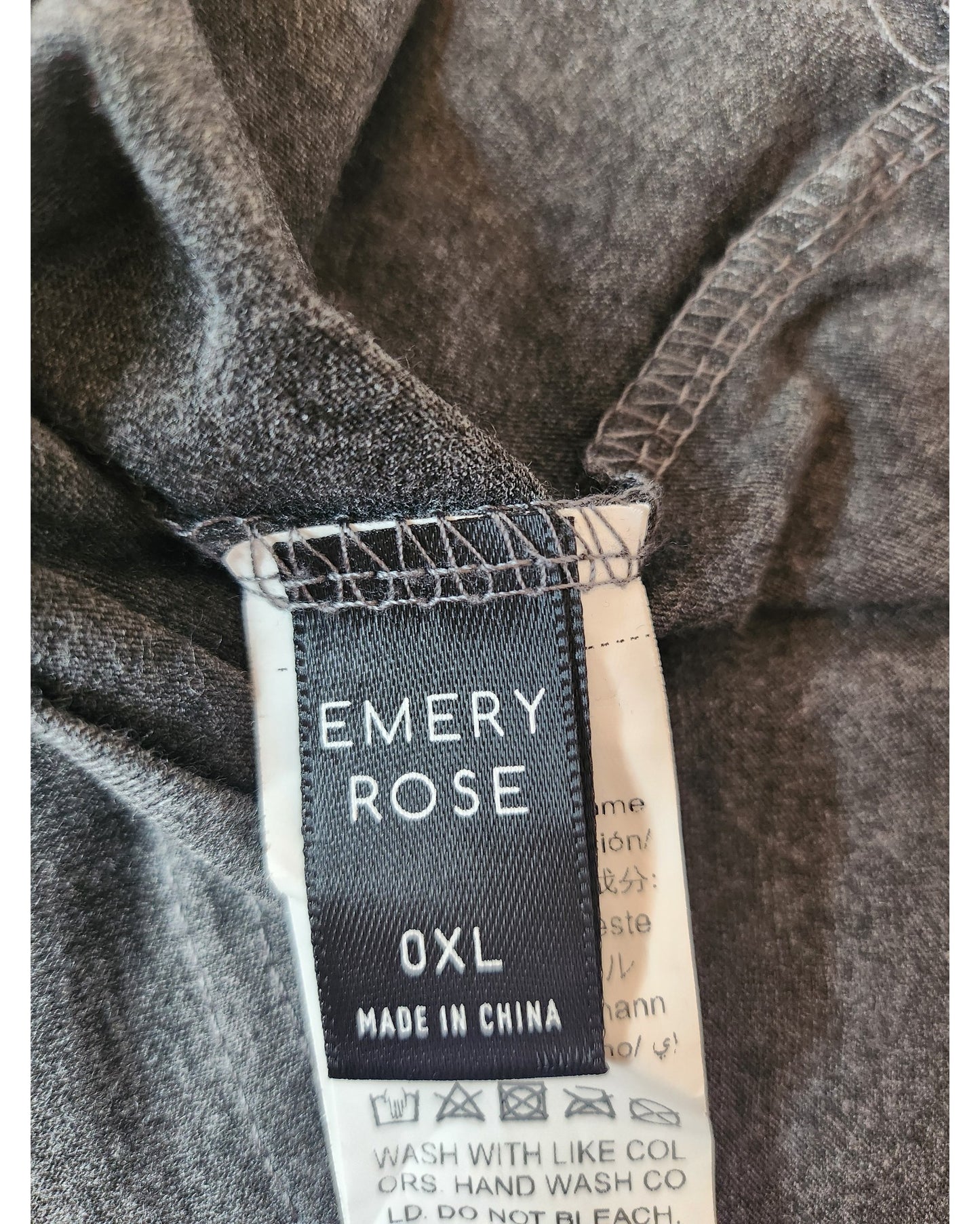 A close-up of a clothing tag on gray fabric from Emery Roses upcycled Breastfeeding & Pumping Mama t-shirt, XL, made in China. Ideal for fans of preloved fashion. Laundry care instructions partially visible below the label.