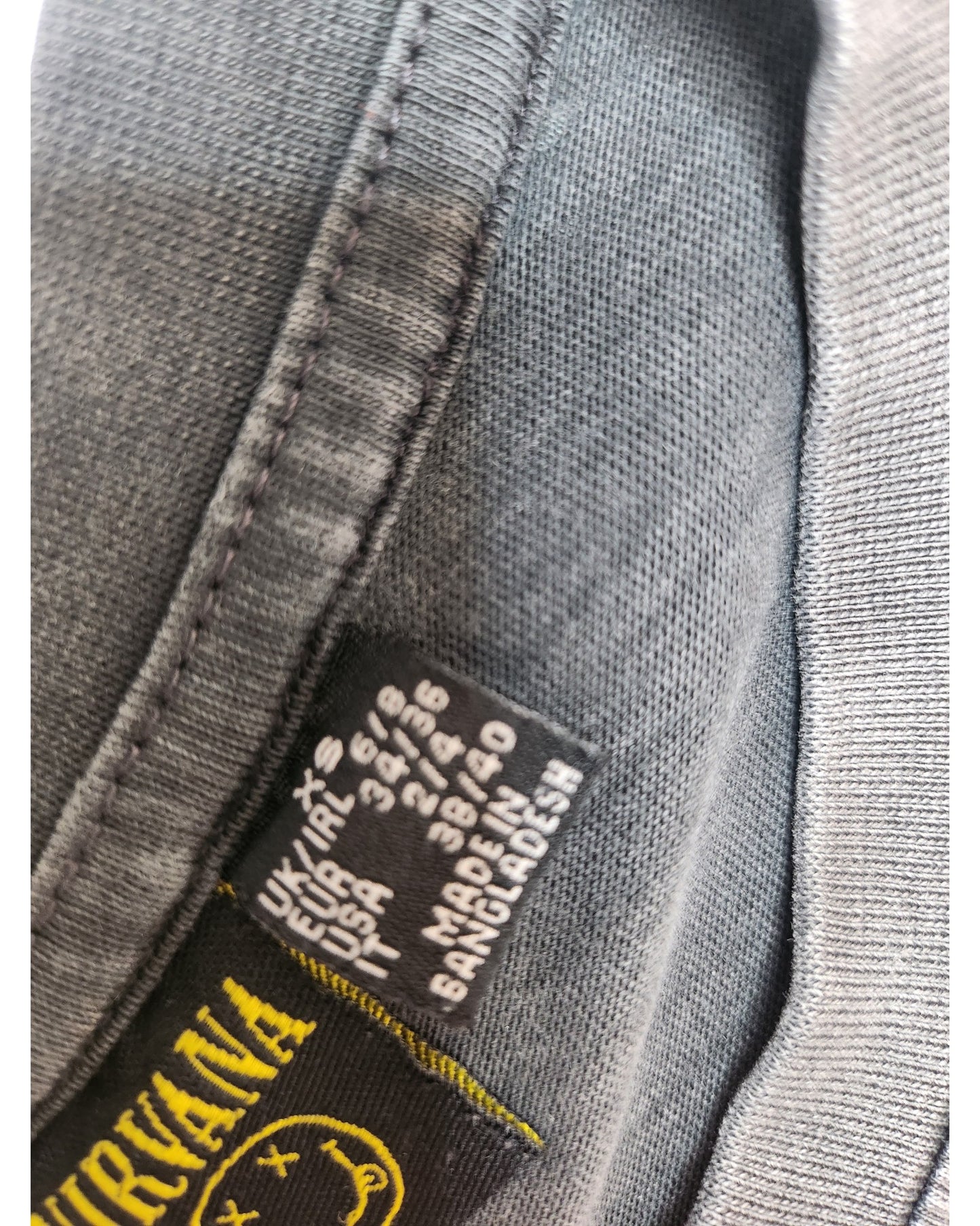 Close-up of a black clothing tag on a Primark Upcycled Breastfeeding & Pumping Dark Grey/Red Floral Nirvana Band t-shirt XS (UK6/8), with size info and MADE IN BANGLADESH in white text.