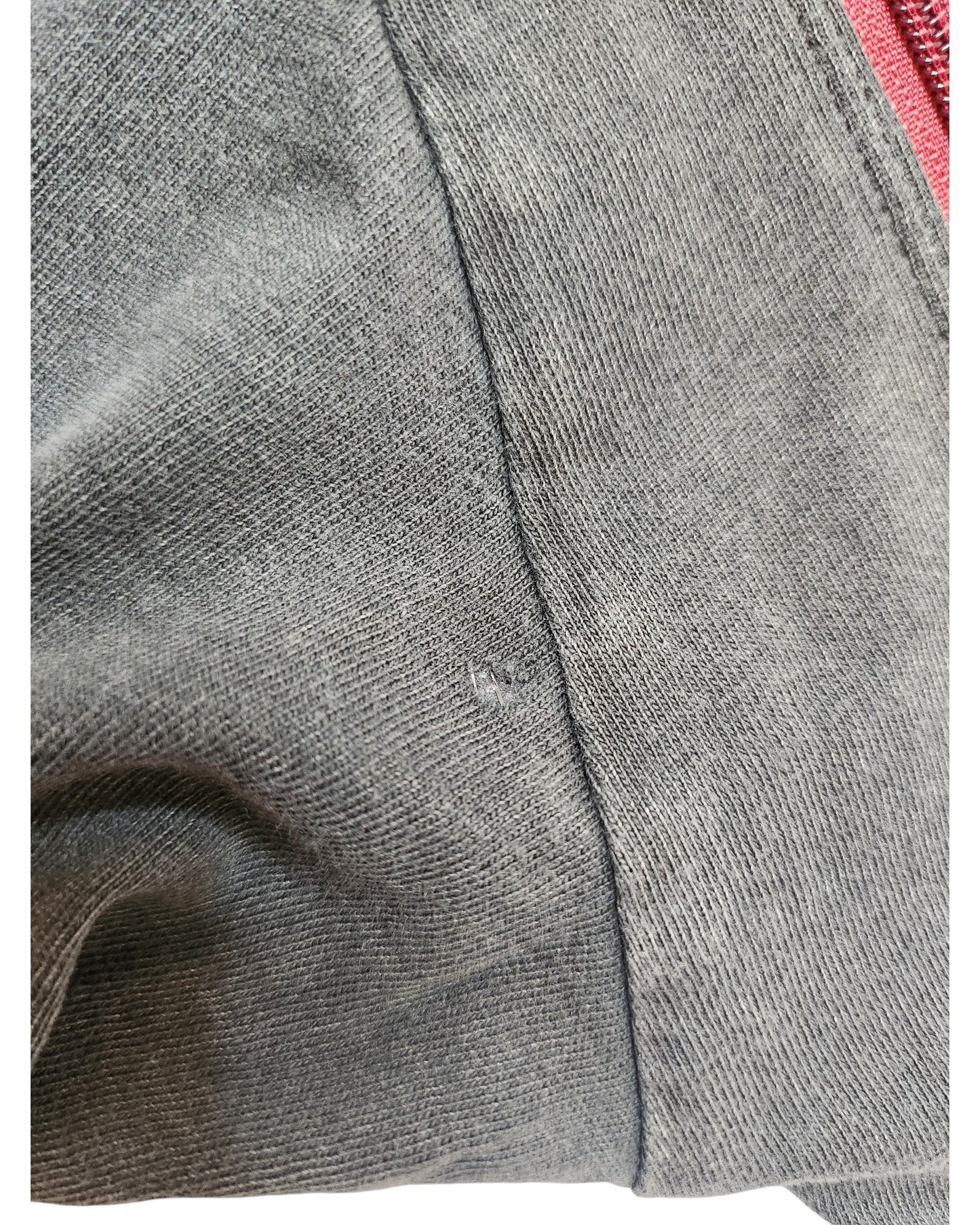 Close-up of a grey fabric with visible stitching and a small hole near the seam, showing the texture of this eco-friendly Primark Upcycled Breastfeeding & Pumping Dark Grey/Red Floral Nirvana Band t-shirt (XS UK6/8). Red zipper edge is in the background.