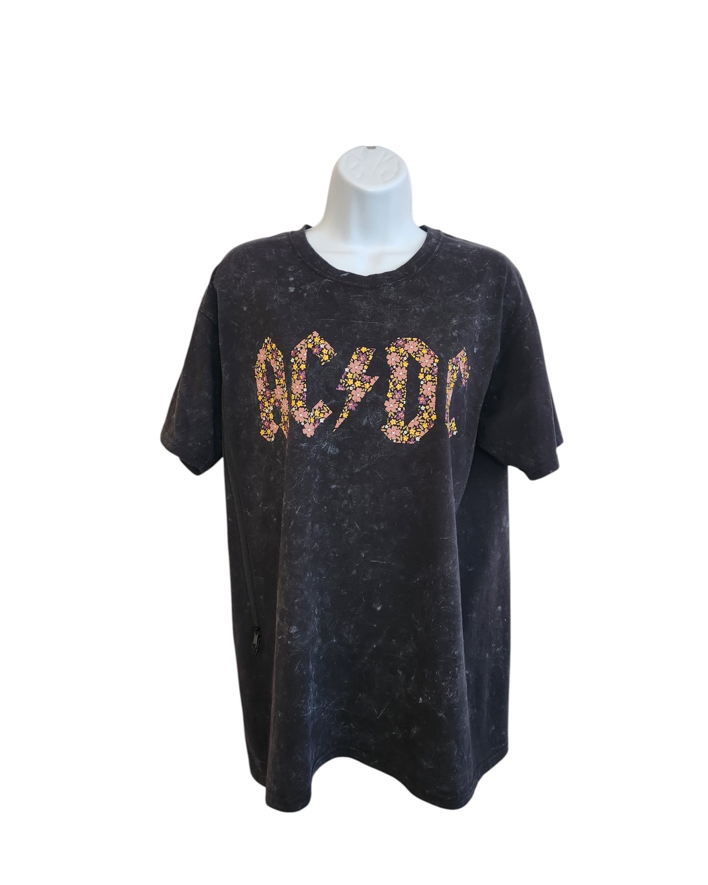 An upcycled, black AC/DC band t-shirt in size M features floral-patterned AC/DC lettering and a faded vintage wash. Designed for breastfeeding and pumping, this preloved shirt offers classic rock style with nursing convenience.