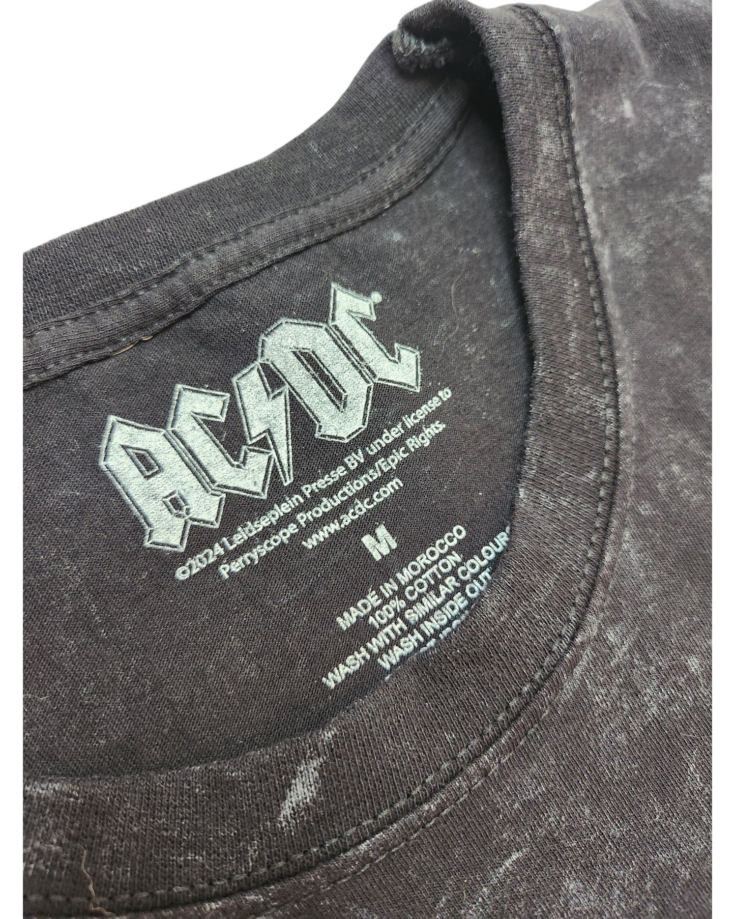 Close-up of an upcycled black AC/DC band T-shirt (size M) from the brand AC/DC, featuring floral details and a nursing/pumping design. The fabric is worn and slightly faded, highlighting the unique character of preloved clothing.