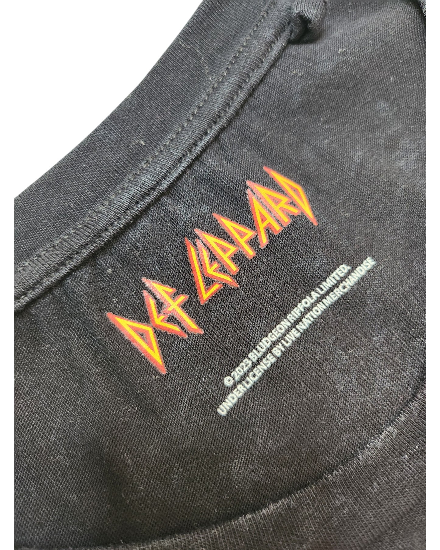Close-up of the black Upcycled Breastfeeding & Pumping Def Leppard Band t-shirt (L) by Def Leppard, featuring the band logo in red and yellow on the collar with white copyright text below. Made from eco-friendly, upcycled materials for sustainable style.