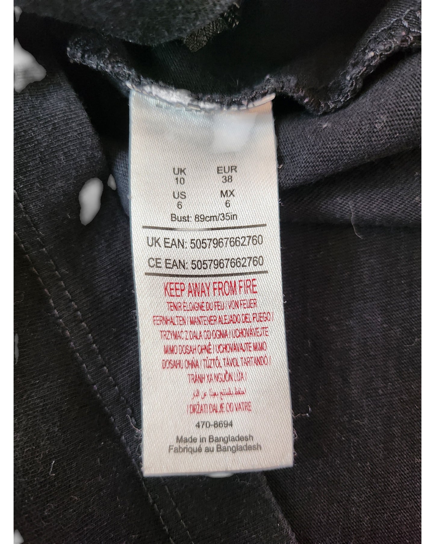 A close-up of the Summer of Rock Upcycled Breastfeeding & Pumping The Beatles t-shirt (UK10) label sewn into black fabric shows multi-region sizes, care instructions, a red fire warning, and notes eco-friendly production in Bangladesh.