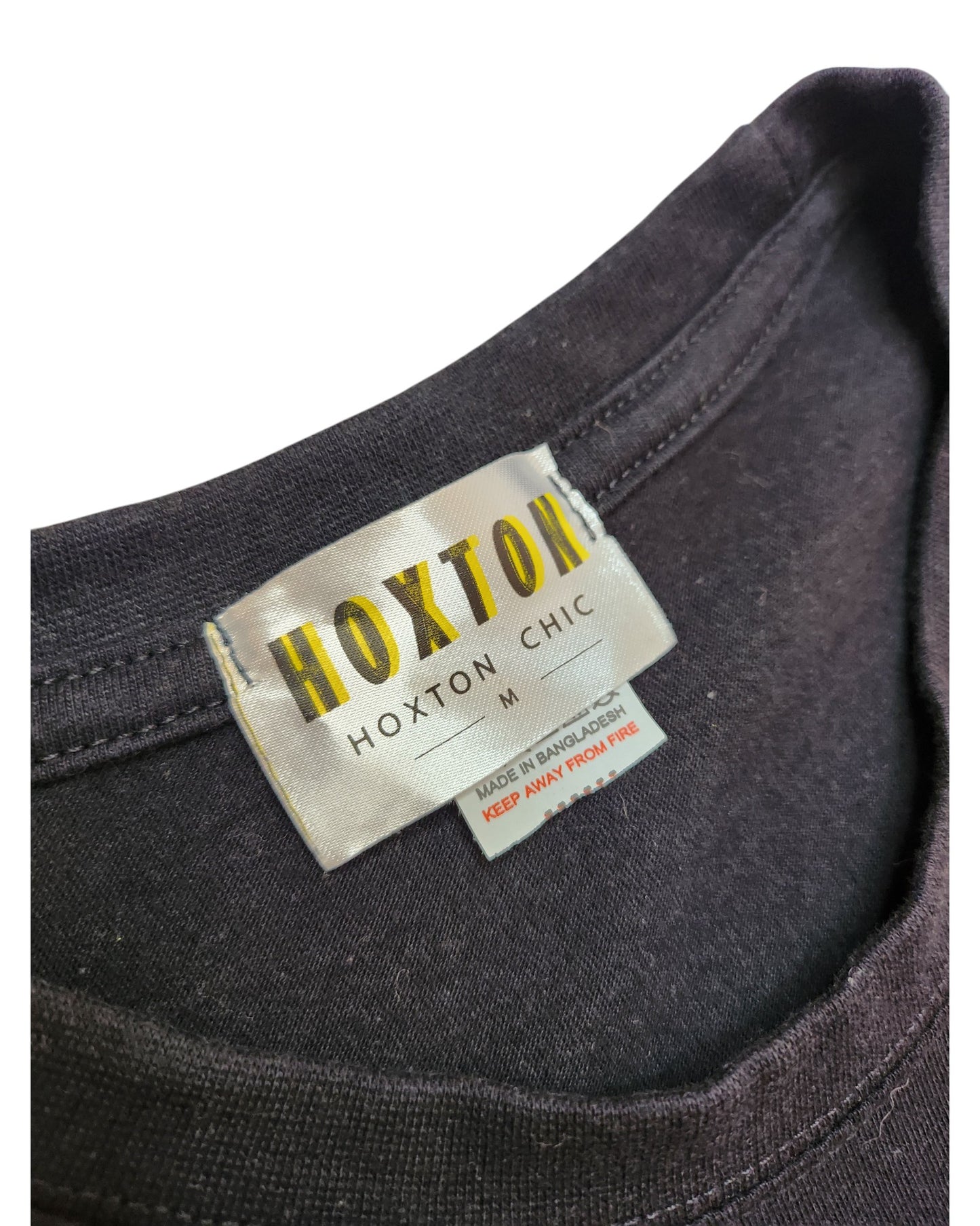 Close-up of a Hoxton Chic label inside a black Upcycled Breastfeeding (Nursing) & Pumping Stop Looking t-shirt M. The smaller tag reads MADE IN BANGLADESH and KEEP AWAY FROM FIRE in red text. Made from eco-friendly, upcycled materials.
