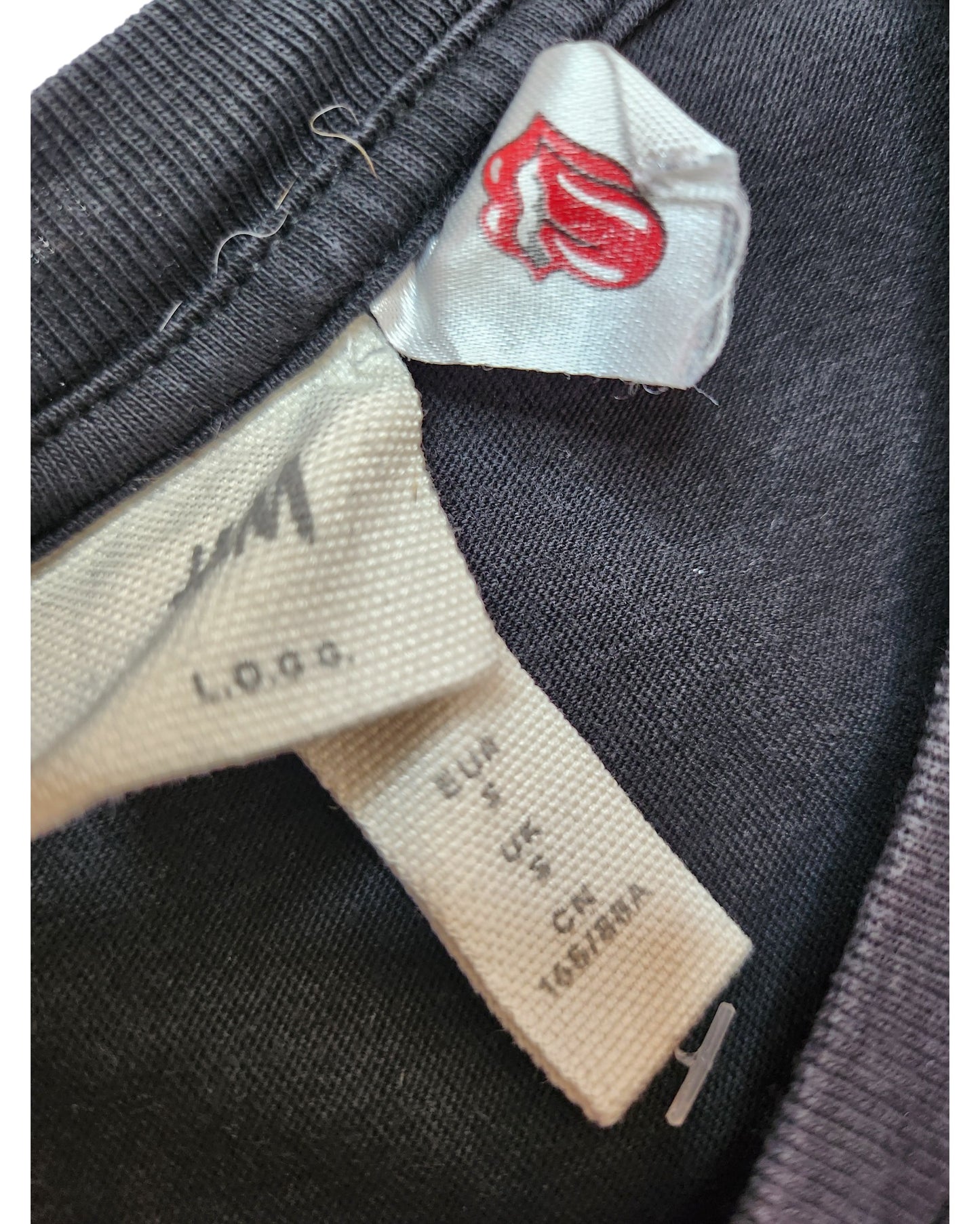 A close-up of two tags on an upcycled H&M Black The Rolling Stones Nursing & Pumping Band t-shirt (size S)—one with the red tongue logo, the other showing H&M branding and care details.