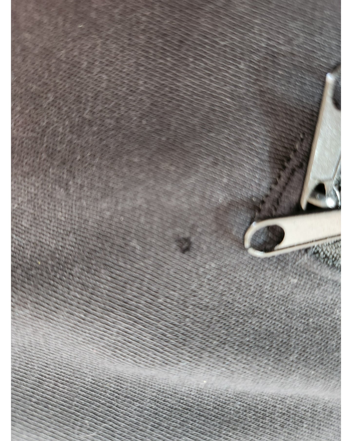 Close-up of the Upcycled Breastfeeding & Pumping Black The Rolling Stones Band t-shirt (size S) by H&M, featuring eco-friendly gray textured fabric with a small dark spot. Metal nail clippers and a file are partially visible in the corner.