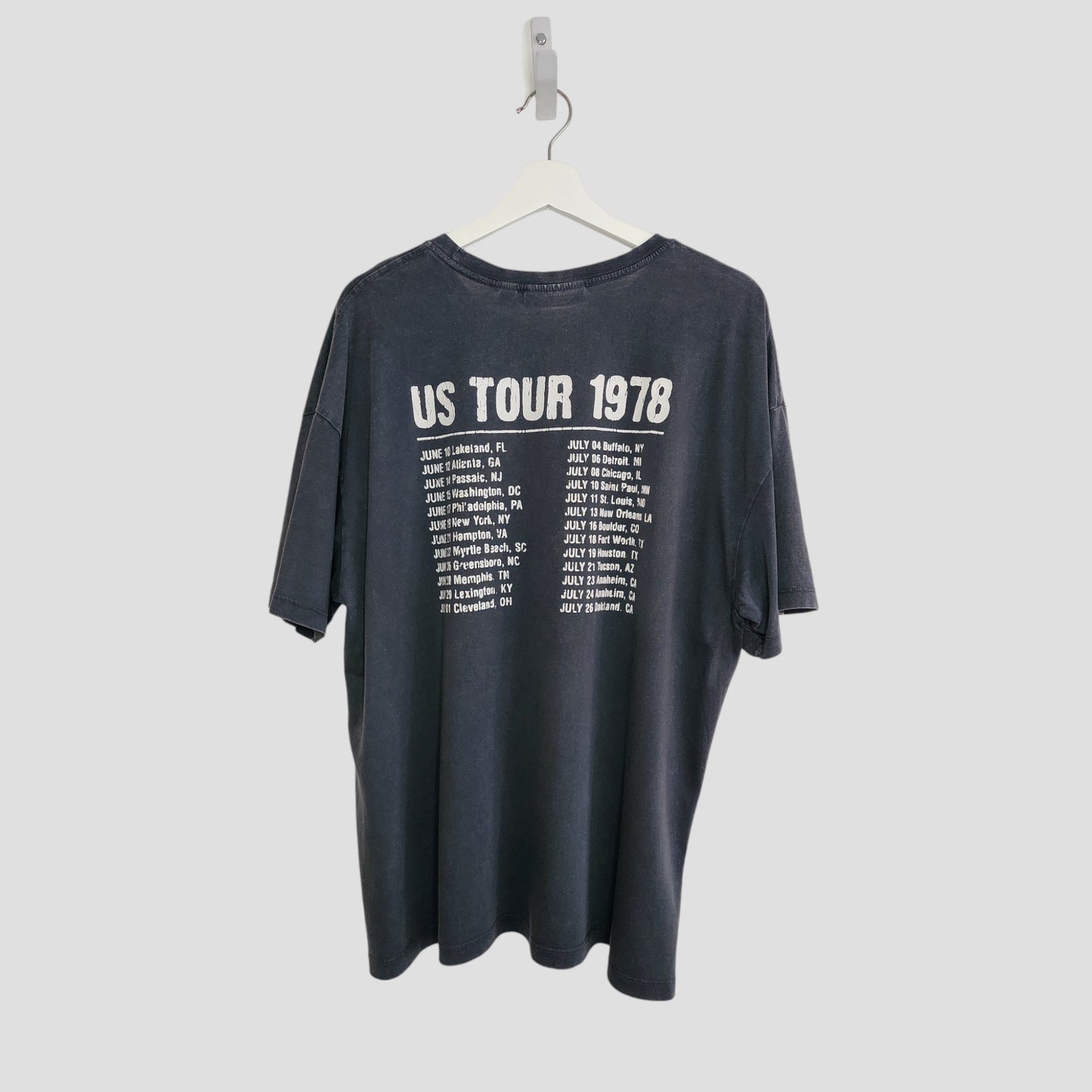 An upcycled black The Rolling Stones US Tour 1978 breastfeeding & pumping t-shirt (size L) hangs on a white hanger; the back features US TOUR 1978 in white with cities and dates, echoing a classic concert tee.
