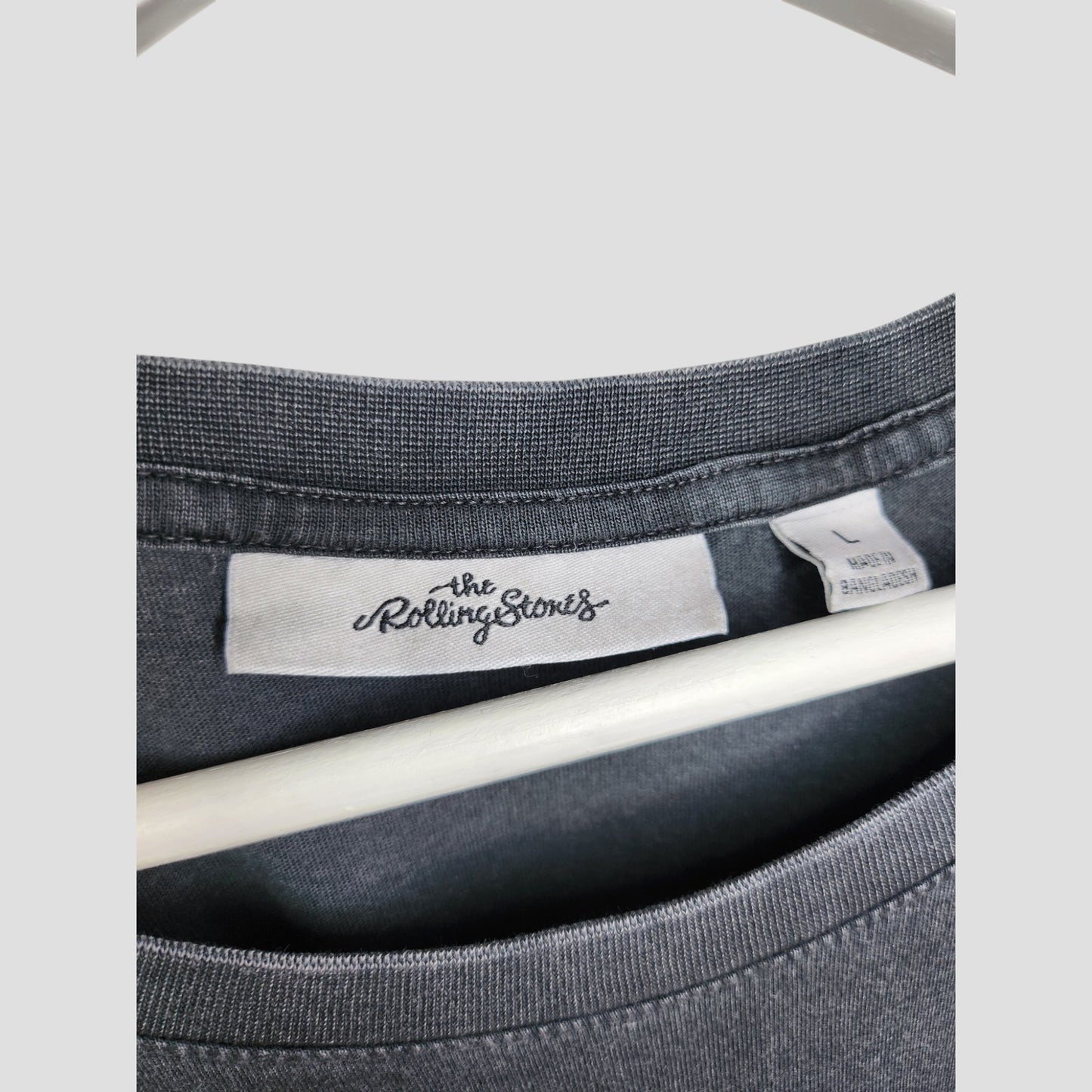 Close-up of a gray Upcycled Breastfeeding & Pumping The Rolling Stones US t-shirt (size L) on a hanger, showing the inside label with The Rolling Stones logo and a tag noting it was made in Bangladesh.
