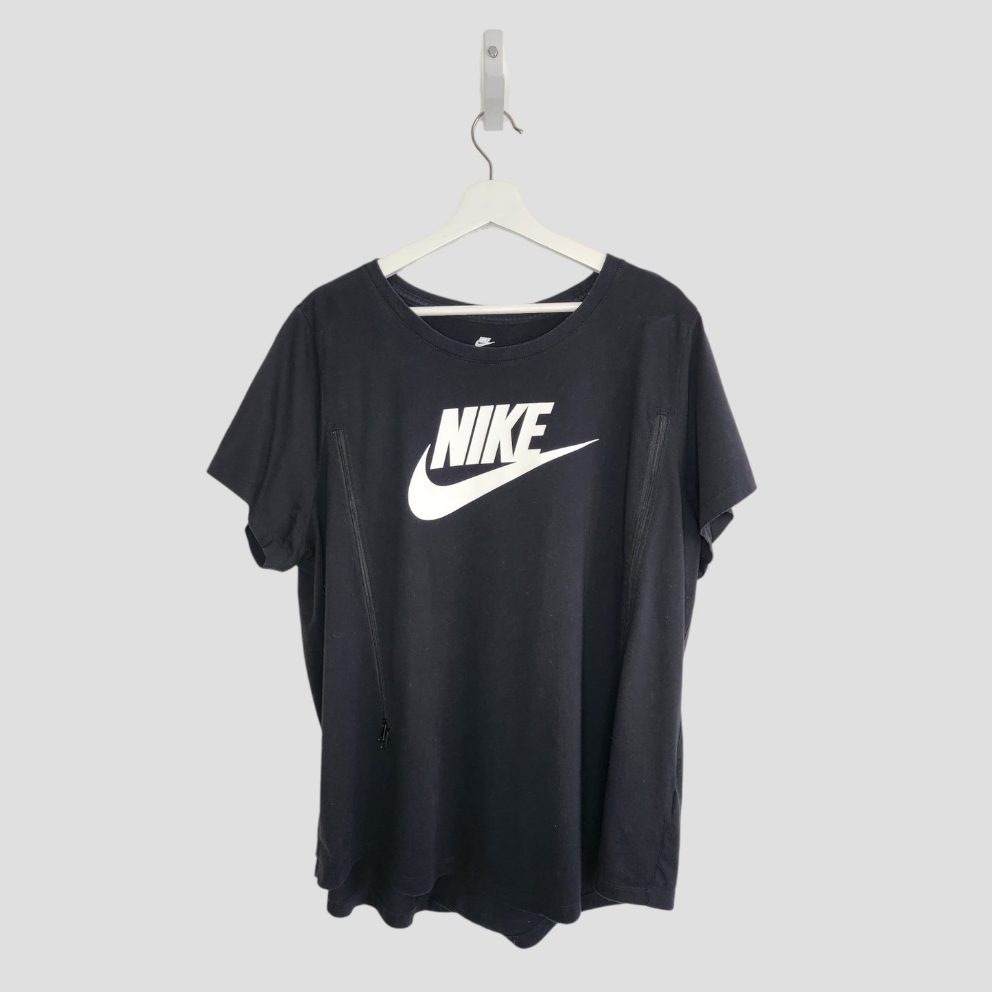 An upcycled XXL black Nike t-shirt for breastfeeding and pumping, featuring a large white Nike logo and swoosh on the front, hangs on a white hanger against a plain light gray background.