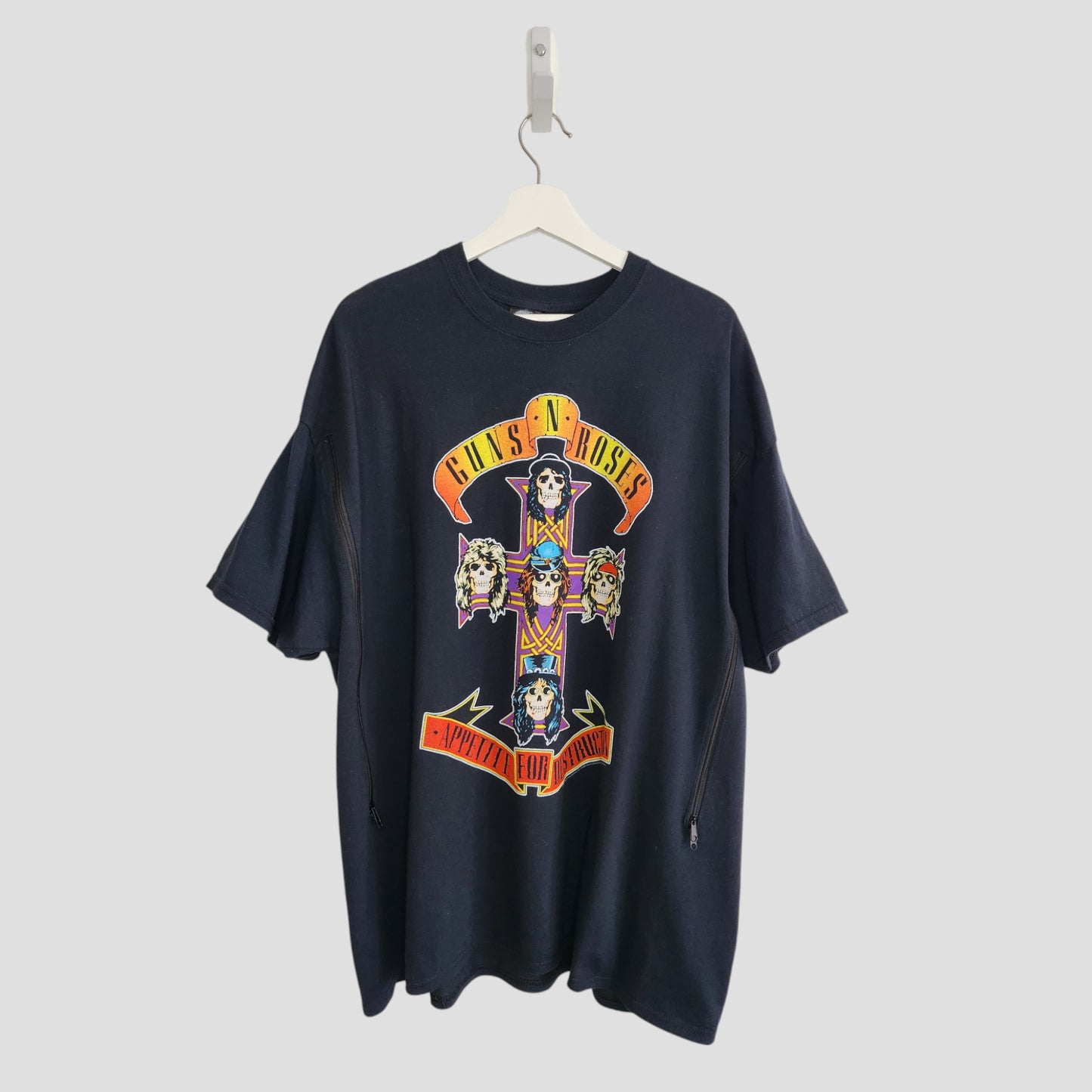An upcycled black XXL GNR Nursing & Pumping T-shirt hangs on a white hanger, showcasing the Appetite for Destruction album cover with cartoon skulls in a cross and the bands bold yellow and red logo.