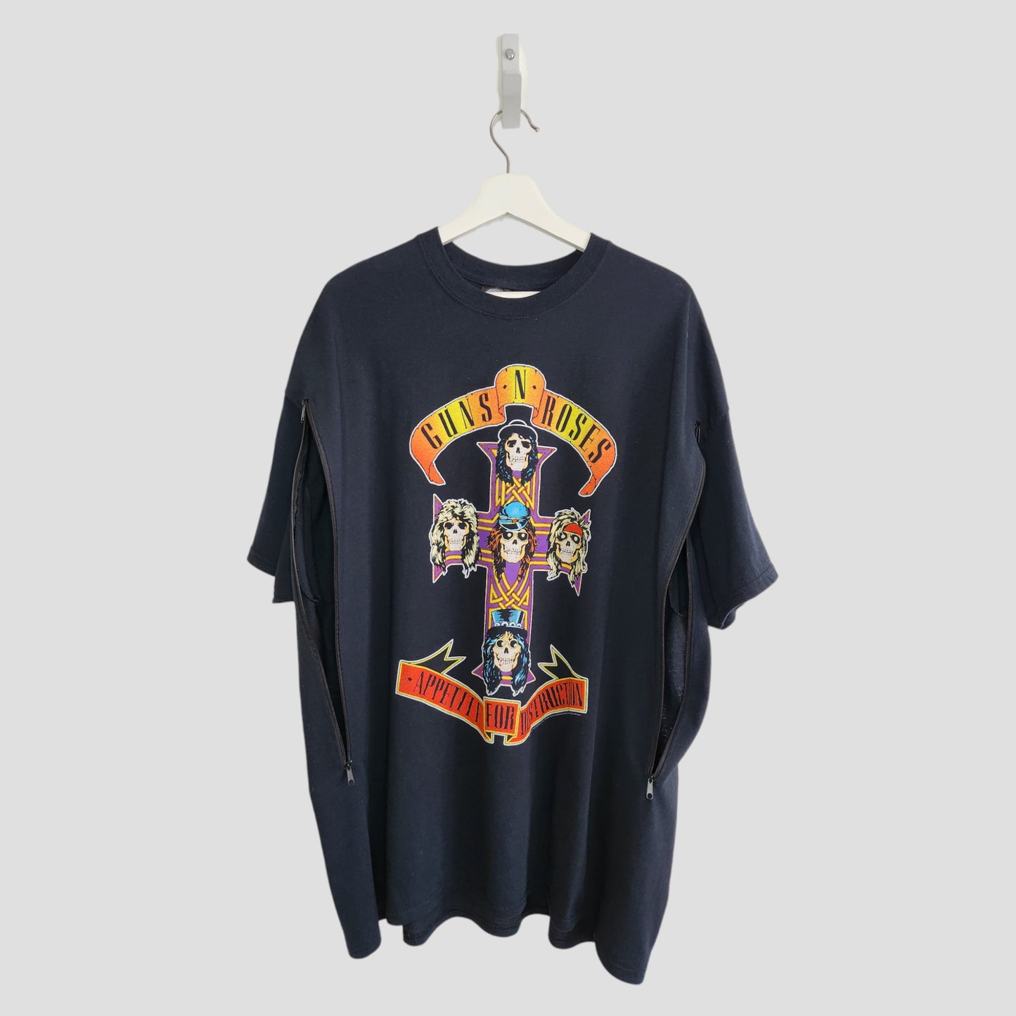 An upcycled black GNR XXL T-shirt for breastfeeding and pumping hangs on a white hanger, featuring colorful cross-and-skull artwork and “Appetite for Destruction” text.