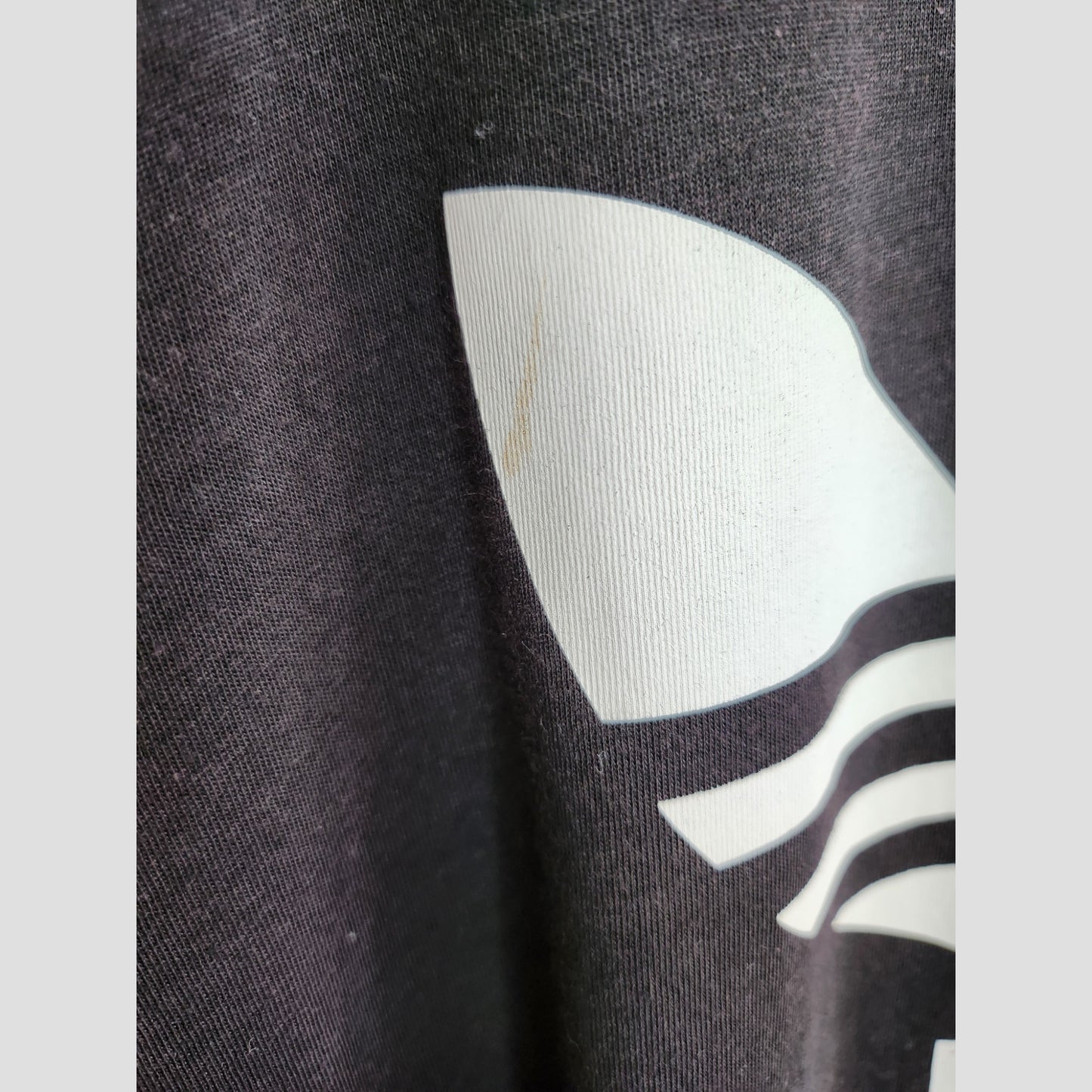 Close-up of the Upcycled Breastfeeding & Pumping Black/White Adidas t-shirt (UK14) shows clear fabric texture, white print, and a faint brown stain near the design. Brand: Adidas.