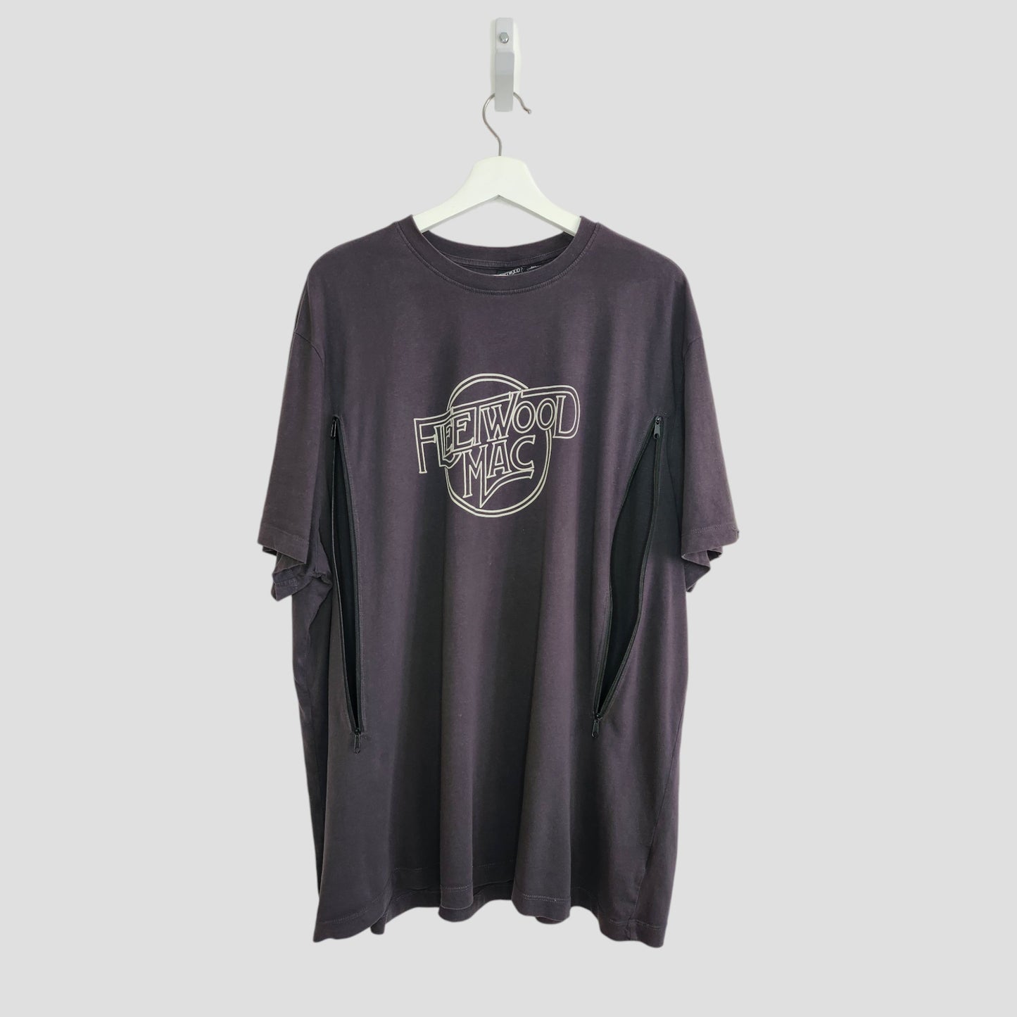 The Primark Upcycled Breastfeeding & Pumping Black/White Fleetwood Mac t-shirt in 3XL, shown on a white hanger against a light gray background, features side zippers for easy nursing—combining style and convenience.