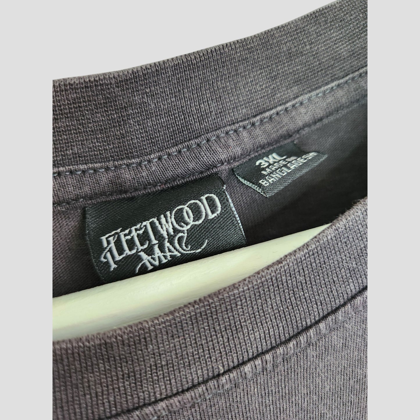 A close-up of a Primark Upcycled Breastfeeding & Pumping Black/White Fleetwood Mac t-shirt in 3XL shows the collar and black label, highlighting eco-friendly fashion with detailed stitching and fabric texture.