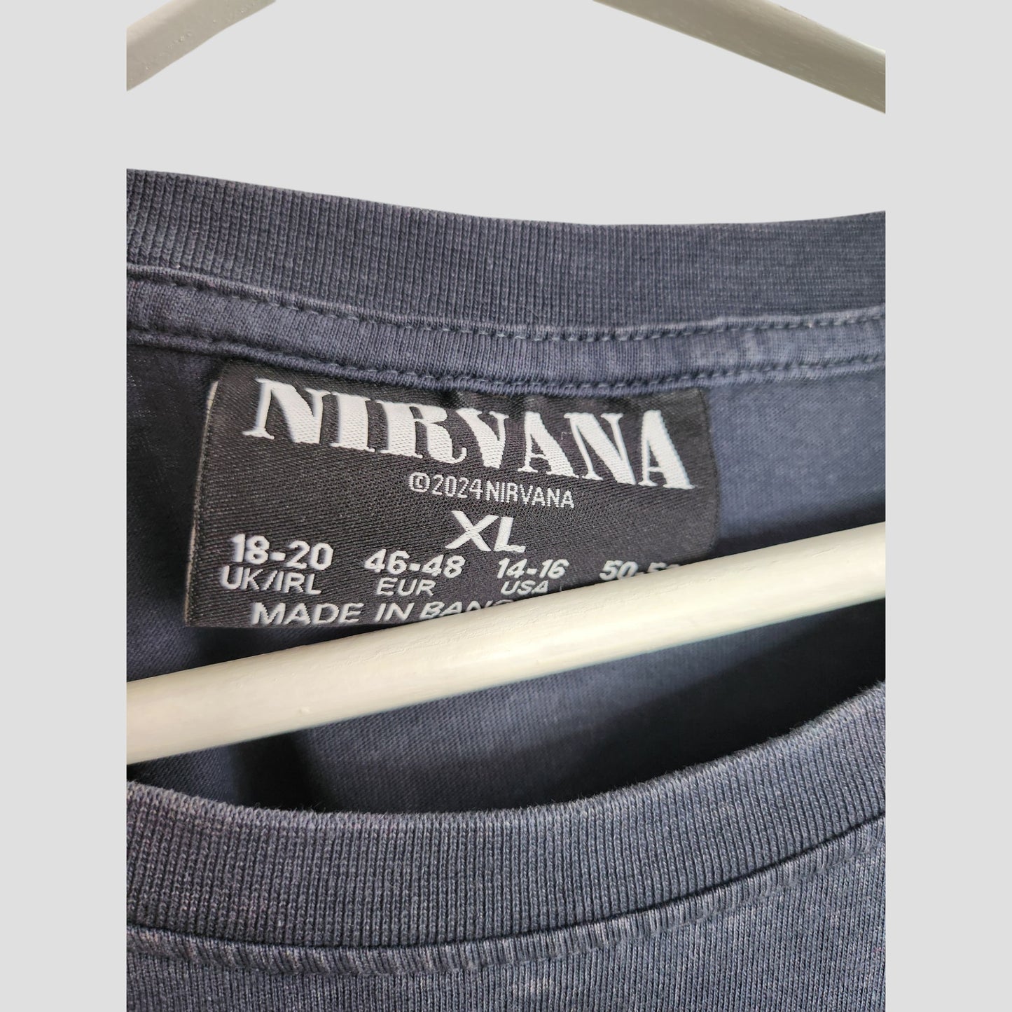 Close-up of a black label inside a Primark Upcycled Breastfeeding & Pumping Grey/Turquoise Nirvana Angel Band t-shirt, size XL (UK18/20), made in Bangladesh. This preloved item hangs on a white hanger.