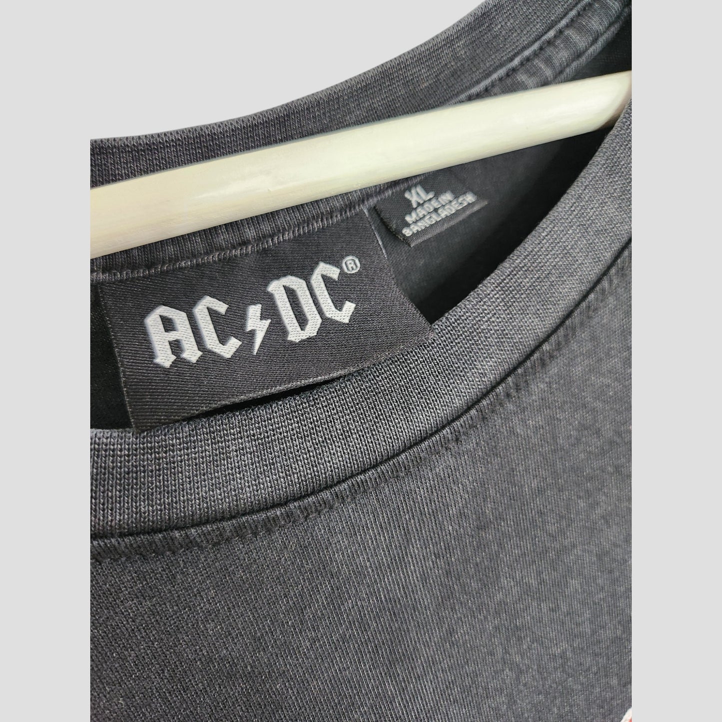 Close-up of a Primark Upcycled Breastfeeding & Pumping AC/DC Faces T-shirt dress (XL, UK18/20) hanging on a hanger, showing the band’s logo label—an ideal eco-friendly choice for music-loving moms.