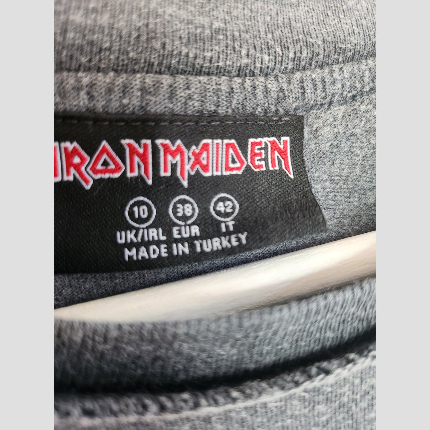 Close-up of a Primark label on grey fabric featuring the Iron Maiden logo, showing sizes UK 10, EUR 38, IT 42. This upcycled breastfeeding & pumping t-shirt (100234) is made in Turkey.