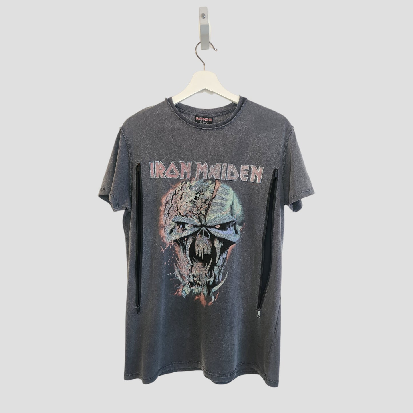 The Primark Upcycled Breastfeeding & Pumping Iron Maiden Band t-shirt UK10 (100234) features a distressed skull graphic on gray fabric—an eco-friendly, unique nursing top for music fans. Shown hanging on a white hanger against a plain light background.