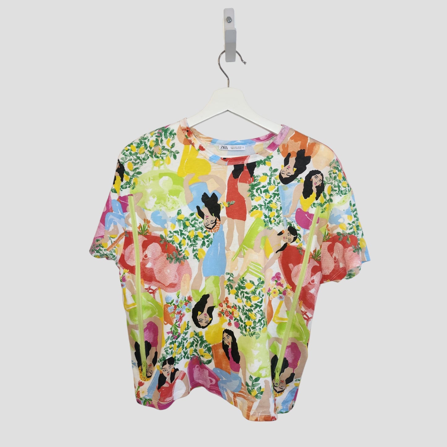 The ZARA Upcycled Breastfeeding & Pumping Girls Printed T-shirt (S) features vibrant abstract women and flowers on soft fabric—an eye-catching, sustainable nursing top displayed on a white hanger against a plain background.
