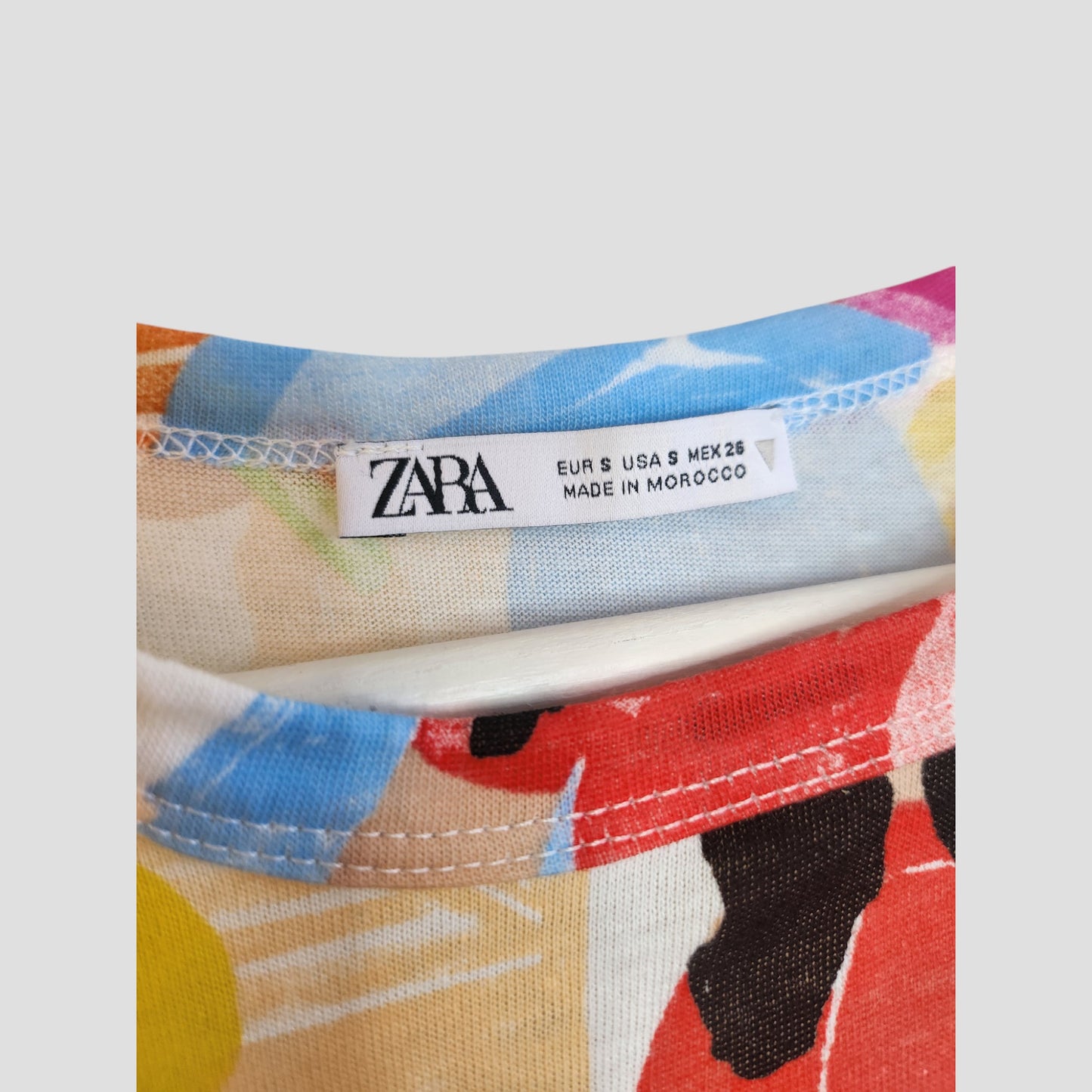 Close-up of the neckline on a ZARA Upcycled Breastfeeding & Pumping Girls Printed t-shirt (S), featuring the ZARA logo and sizing details—a stylish, sustainable choice for eco-friendly nursing wear. Label text: ZARA EUR S USA S MEX 26 MADE IN MOROCCO.