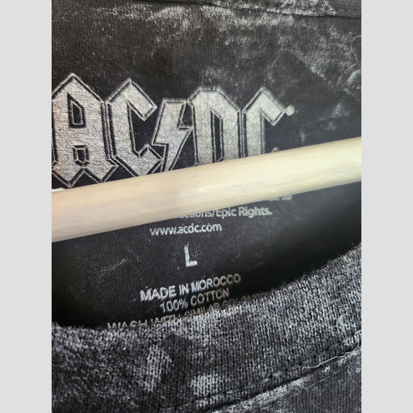 Close-up of an AC/DC black floral band t-shirt, size L (100202), upcycled for breastfeeding and pumping. Made from 100% cotton in Morocco. White logo partially covered by a wooden hanger. Brand: AC/DC.
