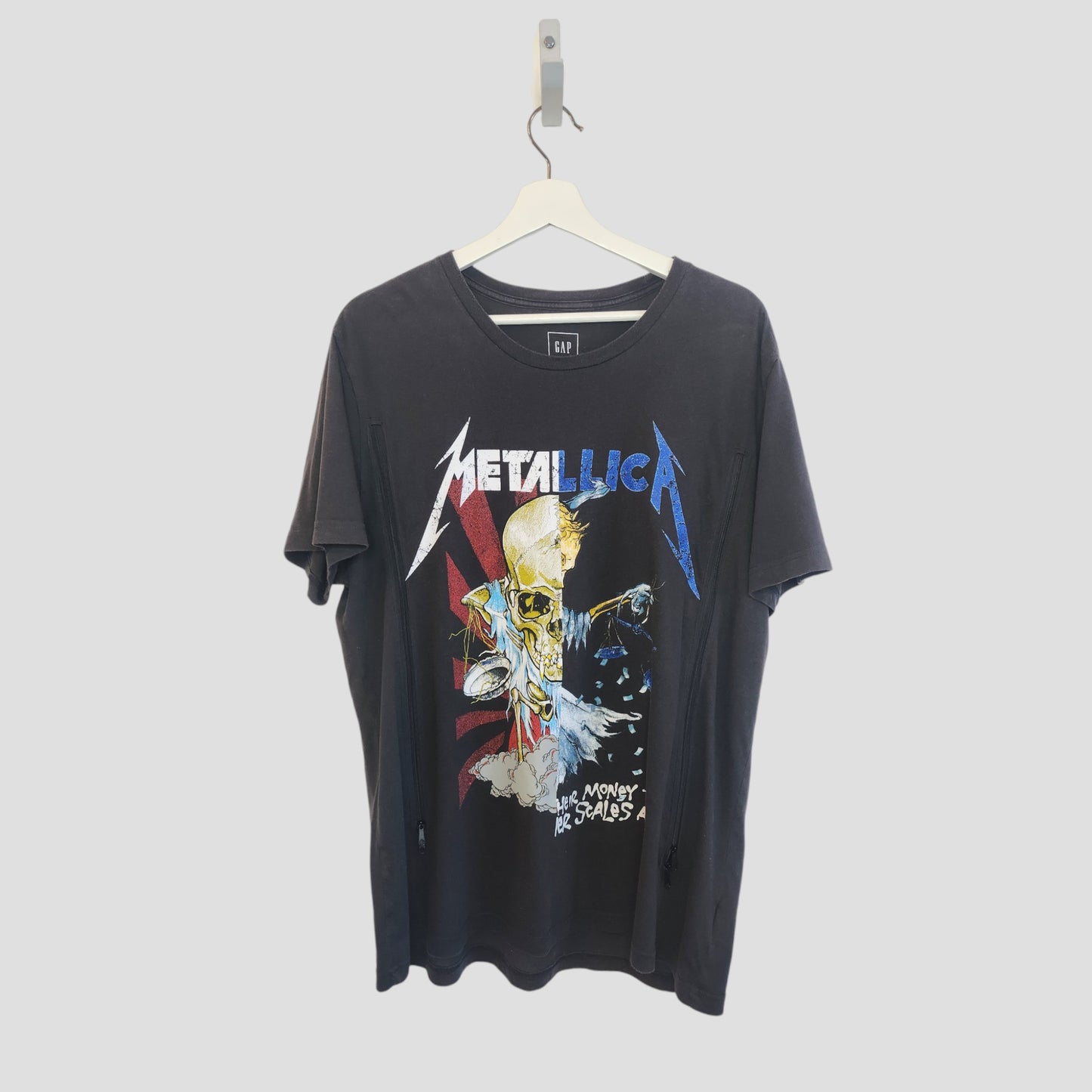A preloved GAP Metallica upcycled breastfeeding and pumping T-shirt (size L) hangs on a white hanger, featuring colorful skull and lightning artwork with the band’s logo across the chest.