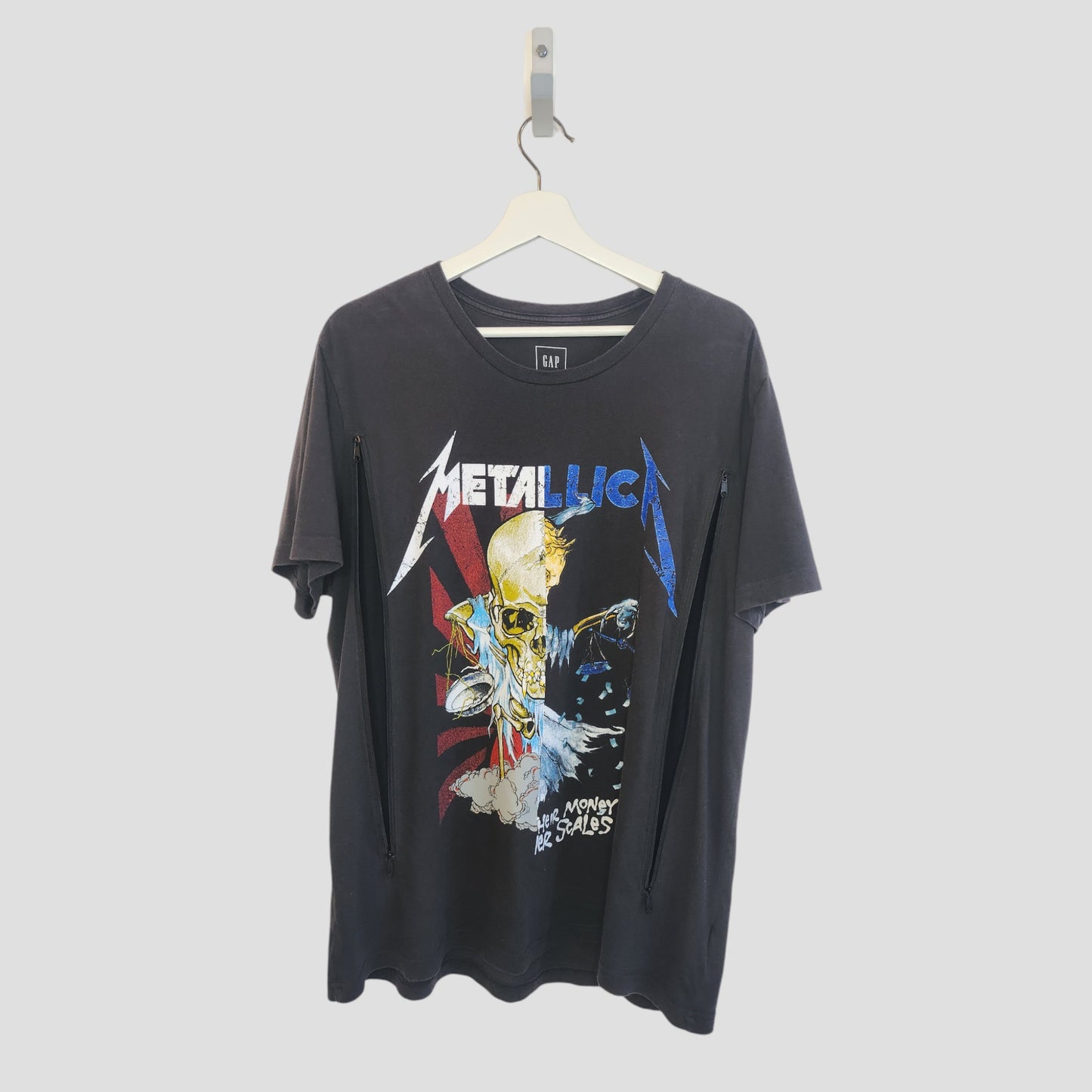 A black upcycled GAP Metallica band t-shirt (L) for nursing and pumping, featuring a colorful skull, lightning bolts, and Metallica ...And Money Be Sales, hangs on a white hanger—perfect for edgy breastfeeding fans.