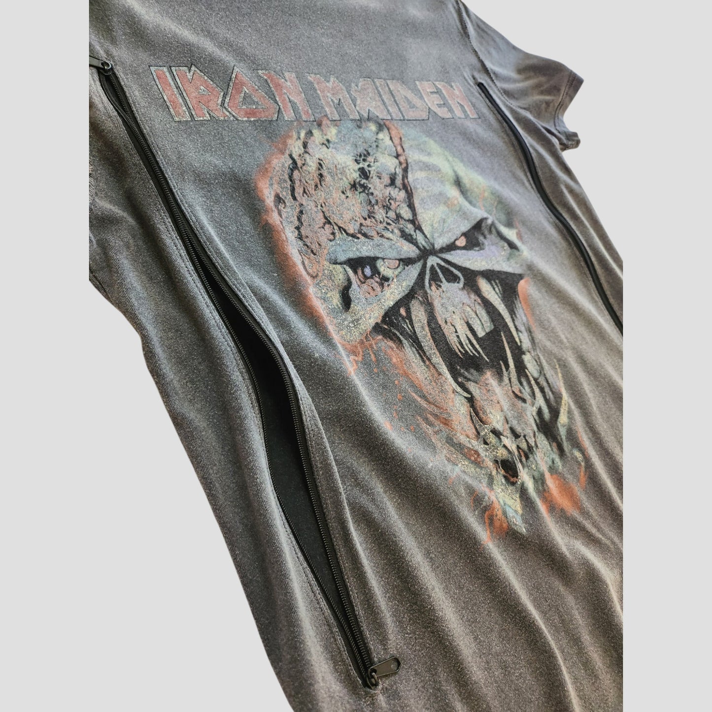 A close-up of a black Primark Iron Maiden t-shirt (UK10, 100234) with a menacing skull and red band logo graphic. This upcycled nursing top features two vertical zippers for breastfeeding or pumping access.