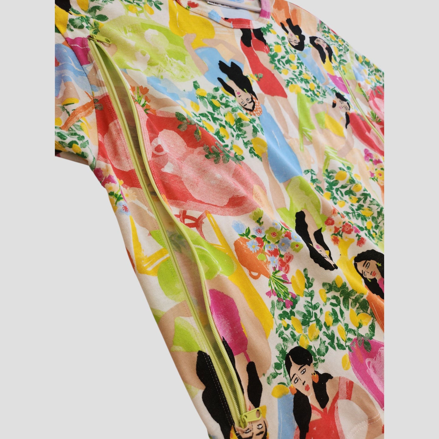 Bright close-up of a ZARA Upcycled Breastfeeding & Pumping Girls Printed t-shirt S, featuring abstract women, plants, bold shapes, and a yellow zipper—crafted from reused nursing clothes for eco-friendly style.