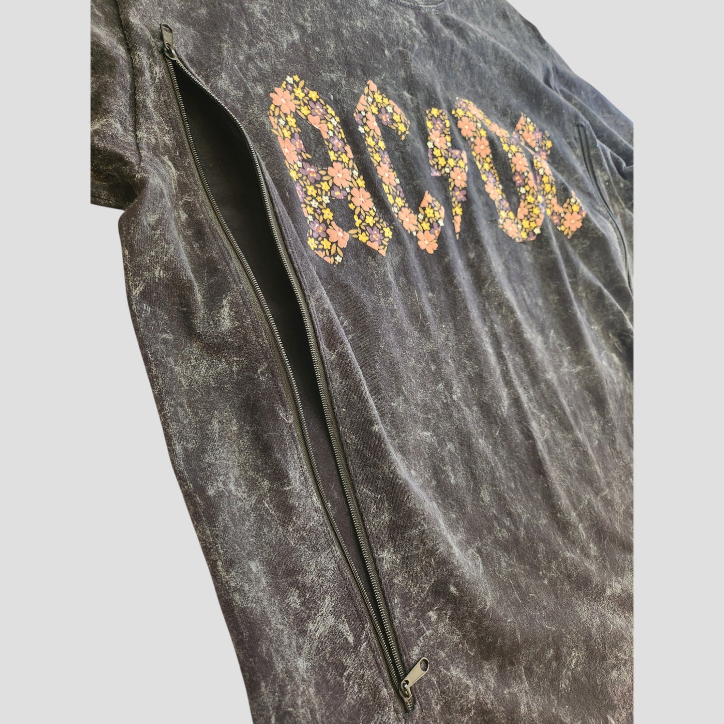 A close-up of the AC/DC Upcycled Breastfeeding & Pumping Black Floral Band t-shirt (L), featuring eco-friendly fabric, a vibrant floral AC/DC print, and a discreet long zipper for nursing and pumping access.