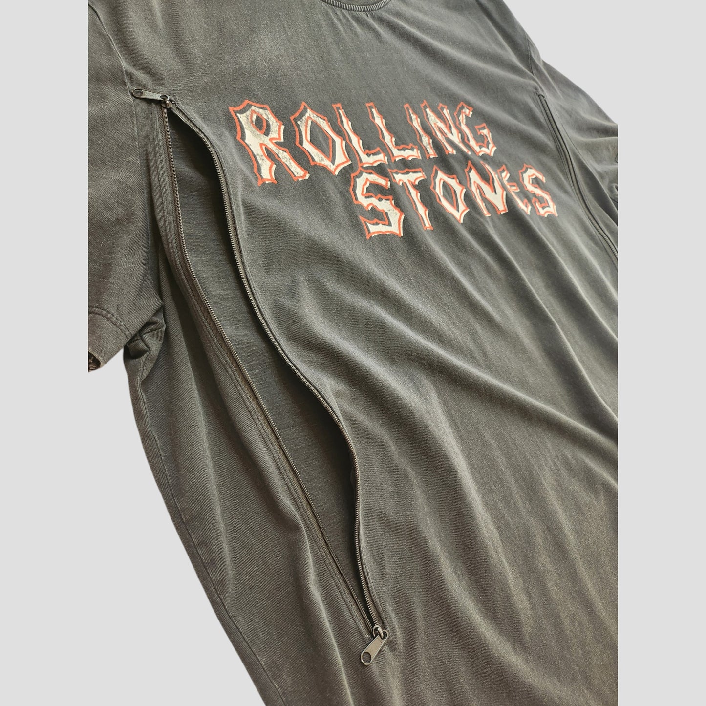 The Primark Upcycled Breastfeeding & Pumping Black Voodoo The Rolling Stones Band T-shirt (XL) features bold, jagged orange ROLLING STONES text and a visible diagonal zipper, made from repurposed nursing wear for an edgy, eco-friendly style.