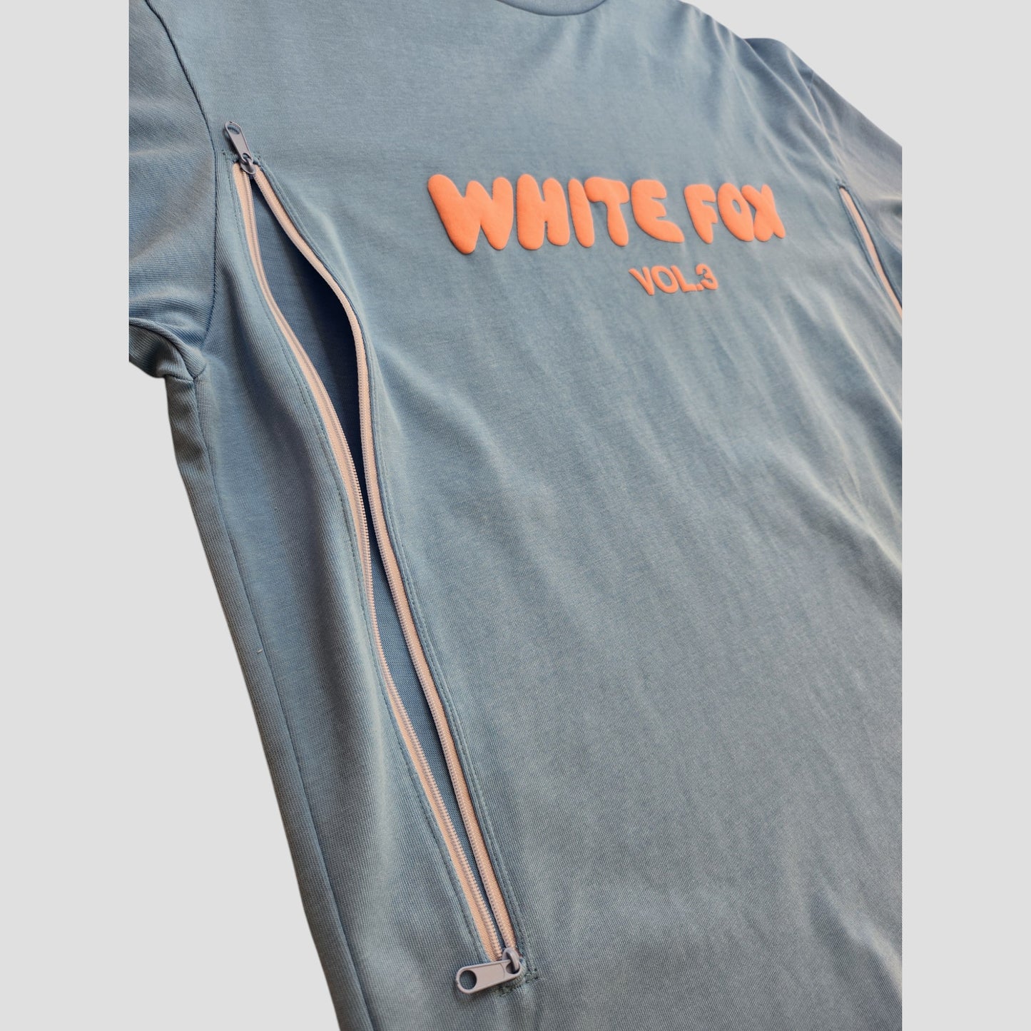The Upcycled Breastfeeding & Pumping Blue White Fox t-shirt M features peach WHITE FOX VOL.3 text on the chest and side zippers, blending functional nursing details with stylish light blue design.