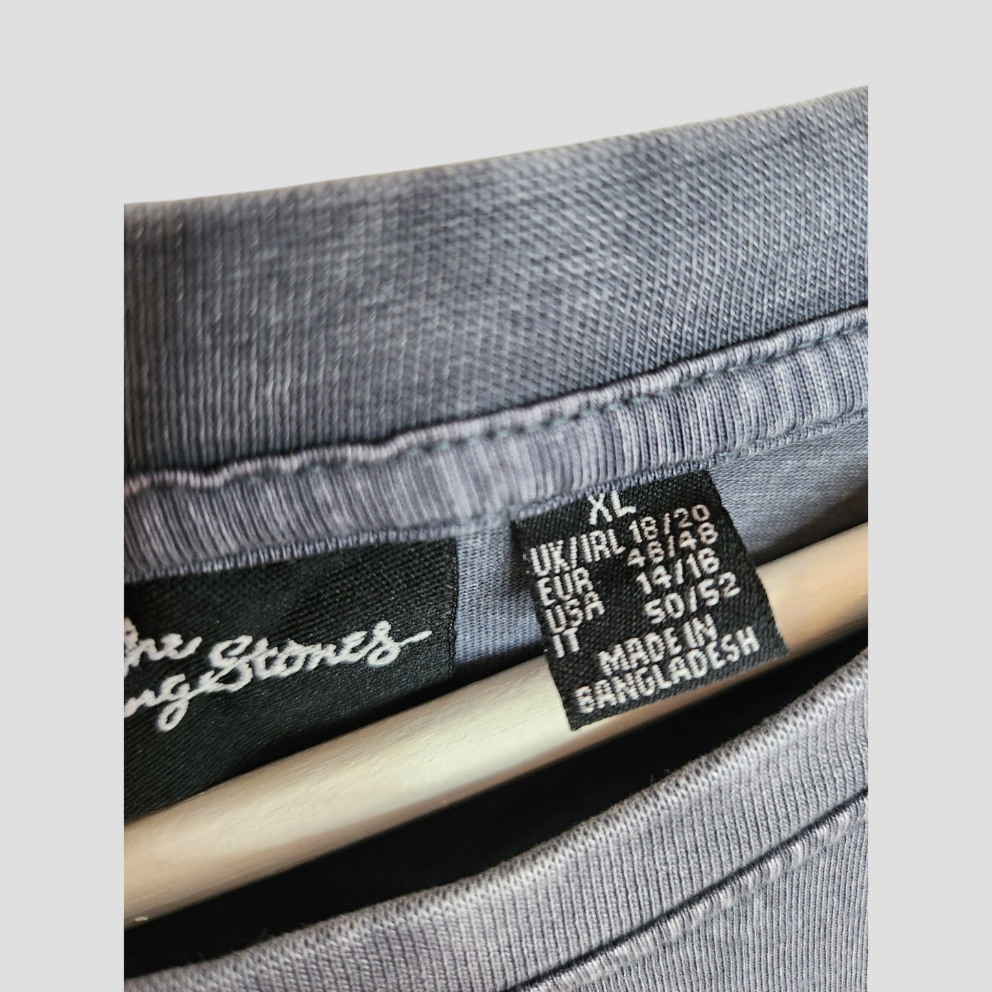 Close-up of a Primark label on the Upcycled Breastfeeding & Pumping Grey/Red Stars The Rolling Stones t-shirt XL (UK18/20), showing size info and MADE IN BANGLADESH, with a hanger visible inside.