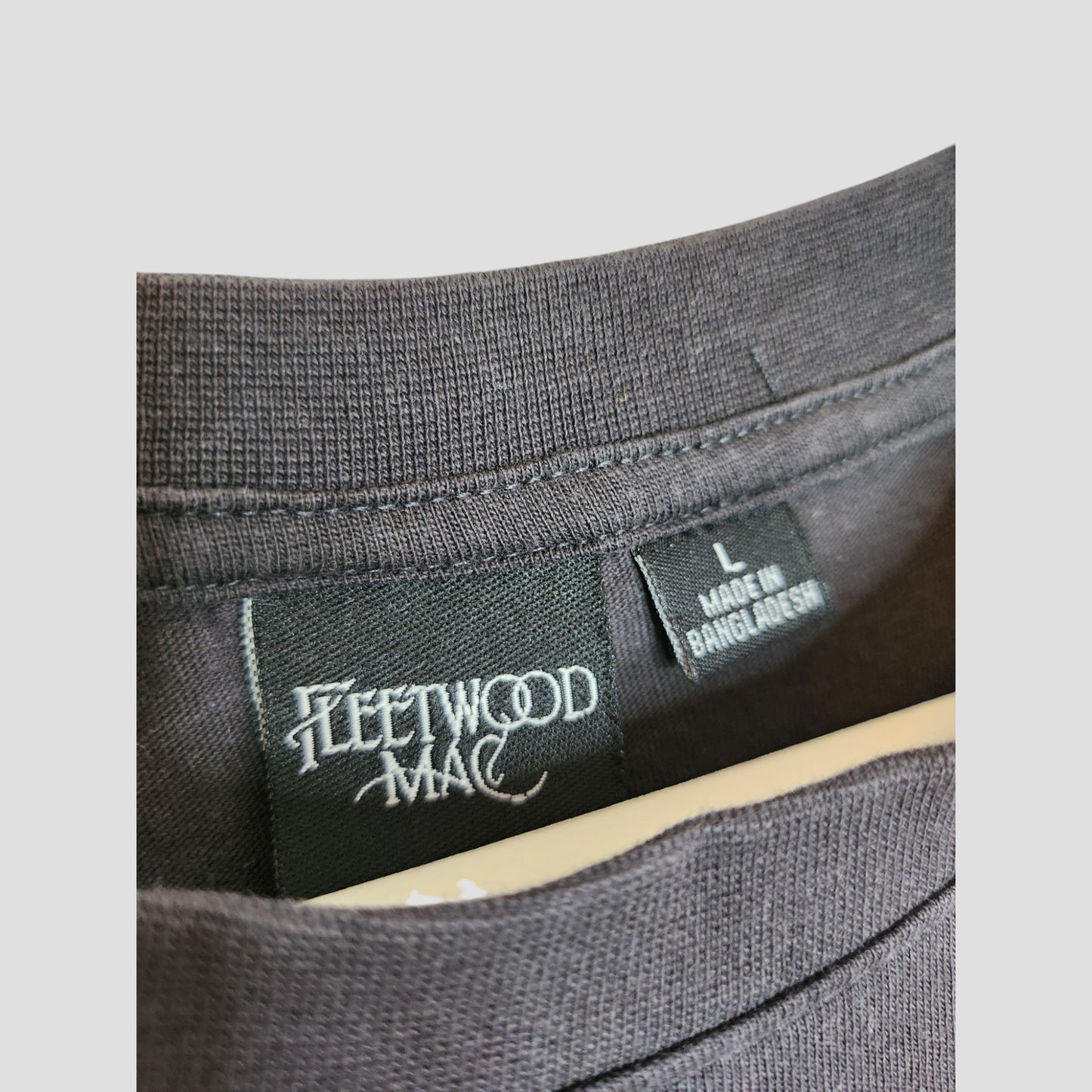 Close-up of a Primark Upcycled Breastfeeding & Pumping Black/White Fleetwood Mac T-shirt (L, UK14/16, 100292), showing two tags—one with the bands name and another with size and origin—perfect for eco-conscious music fans.