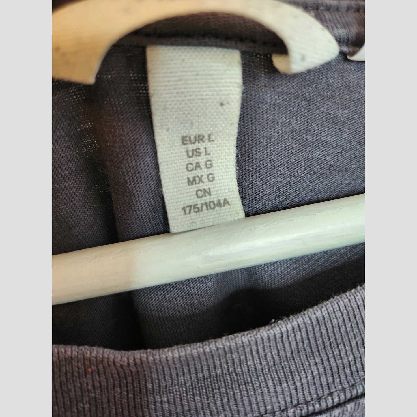 Close-up of a clothing tag stitched inside the back of an H&M Upcycled Breastfeeding & Pumping Grey/Red The Rolling Stones t-shirt (size L, 100297), displayed on a hanger.