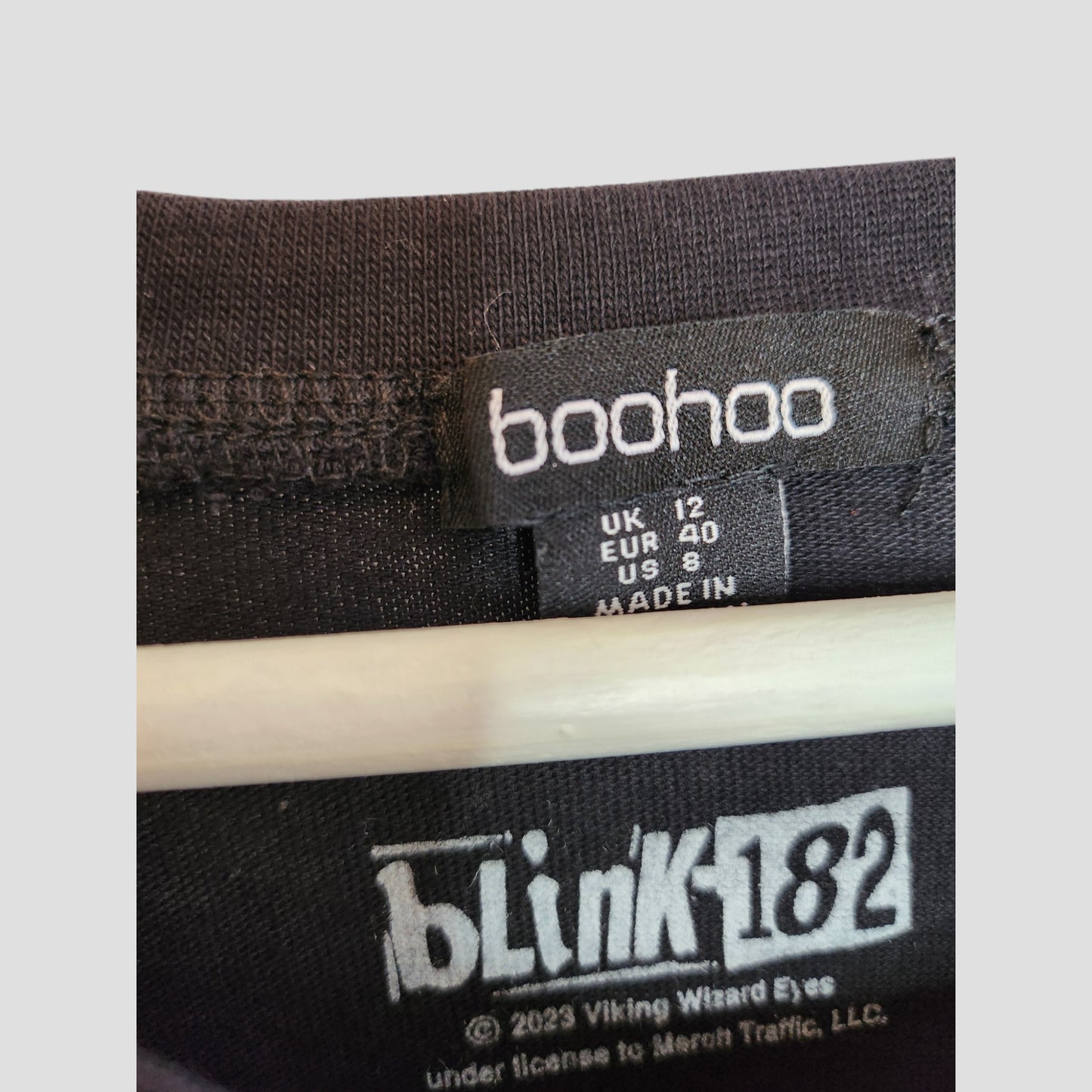 Close-up of a boohoo clothing label with size UK16, partly showing MADE IN. Below, a printed blink-182 logo and licensing details feature on this upcycled breastfeeding & pumping t-shirt—ideal for fans of preloved maternity wear.