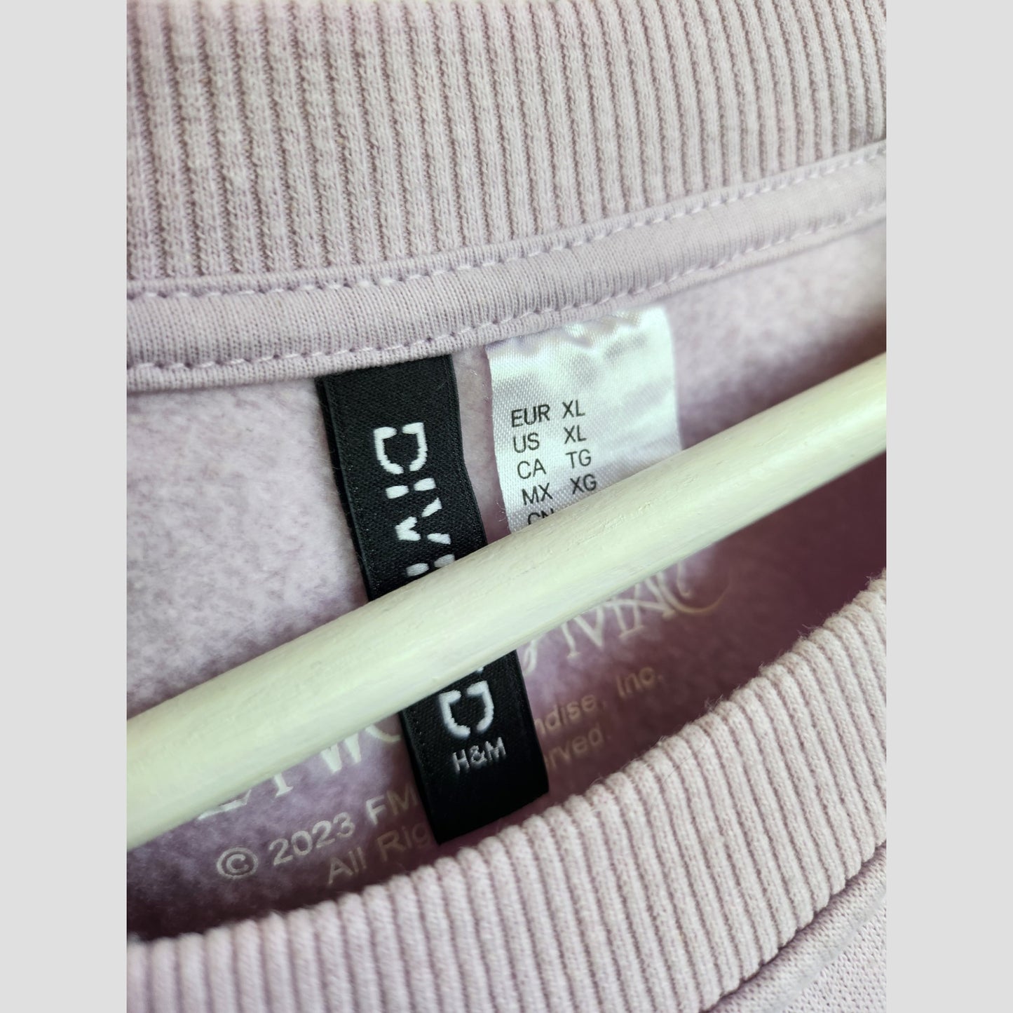 Close-up of the collar and tags on an H&M Upcycled Breastfeeding & Pumping Lilac Fleetwood Mac Band Sweatshirt (XL), showing size labels for various regions—perfect preloved nursing wear blending comfort and style.