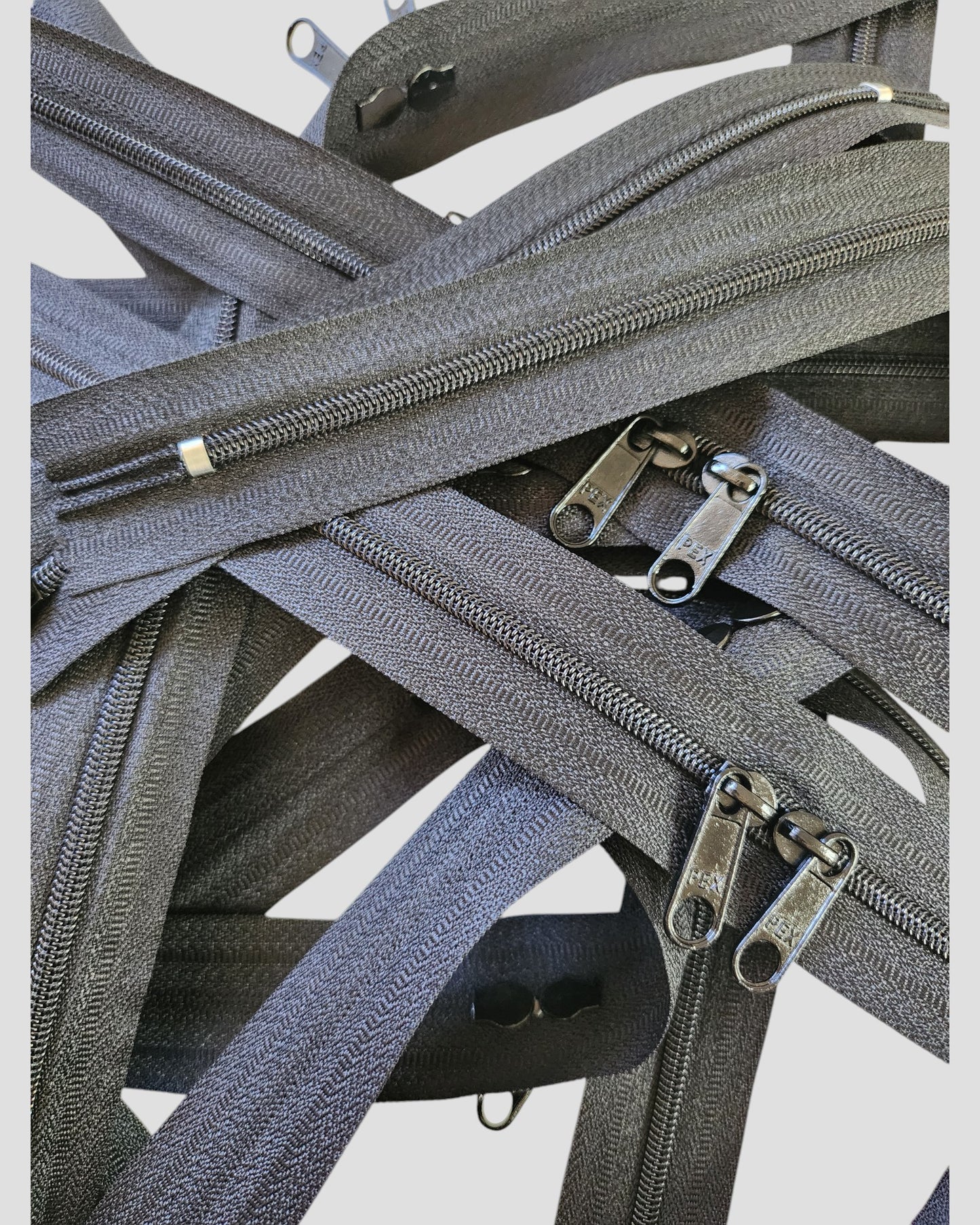 The Original Sew-On Zip Kit by touched out mama features overlapping gray zippers with metal sliders, arranged in a crisscross pattern—ideal for beginner sewing or creative upcycle t-shirt projects.