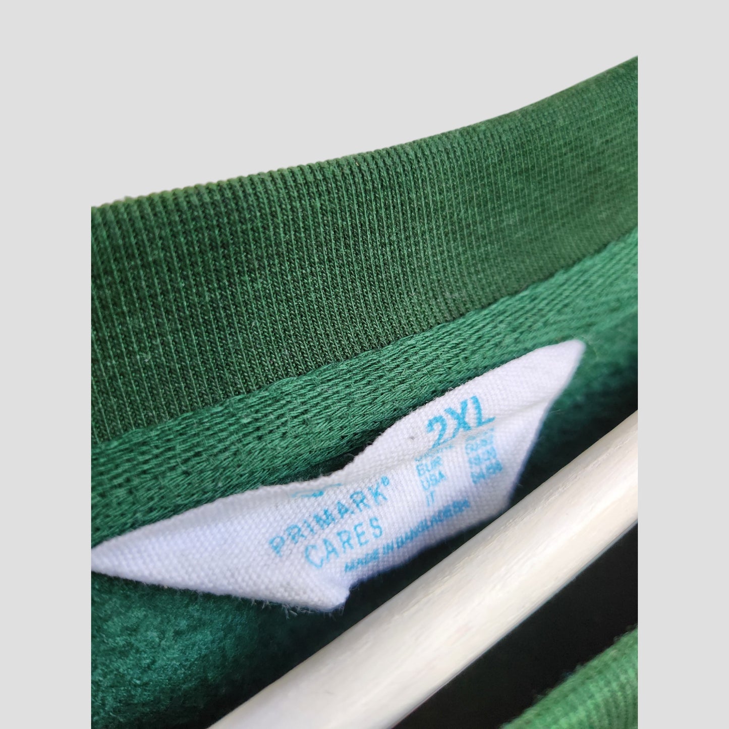 Close-up of a green Primark Upcycled Breastfeeding & Pumping HOHOHO Christmas Lights Sweatshirt, size 2XL, showing the white brand tag. The eco-friendly sweatshirt hangs on a white hanger against a plain background.