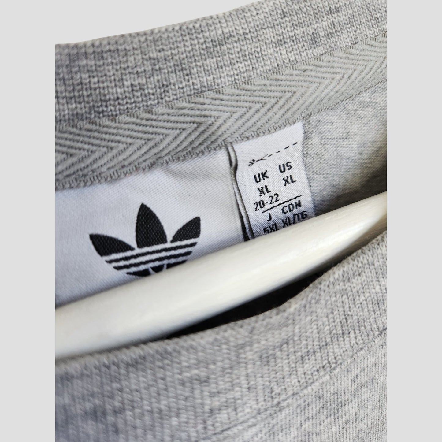 Close-up of an Adidas Originals Upcycled Breastfeeding & Pumping T-shirt (Grey/Green, XL UK20/22), showing the inside collar with sizes and the black trefoil logo. The eco-friendly piece is partially displayed on a white hanger.