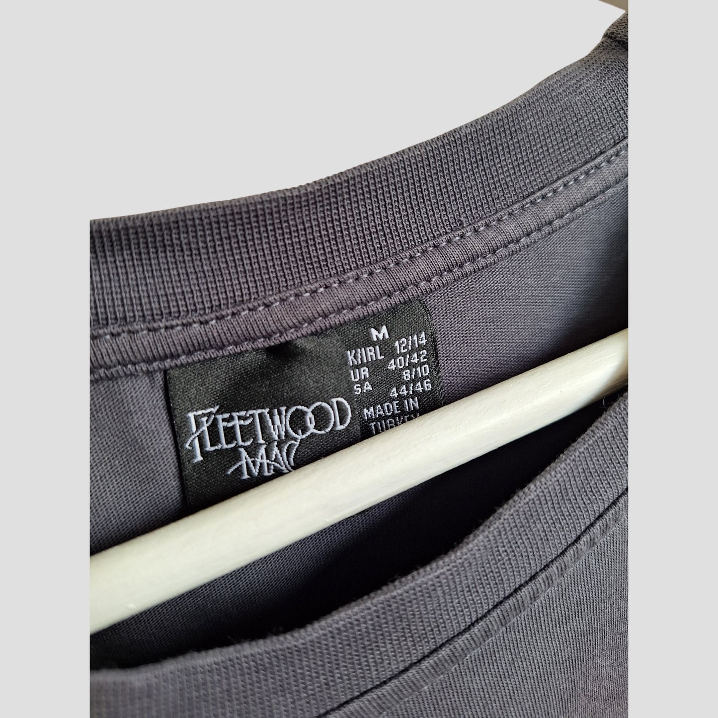 Close-up of a Primark Upcycled Breastfeeding & Pumping Floral Fleetwood Mac Band t-shirt (M/UK12/14), showcasing the logo label, size info, and Made in Turkey—an eco-friendly, stylish pick for music-loving moms.