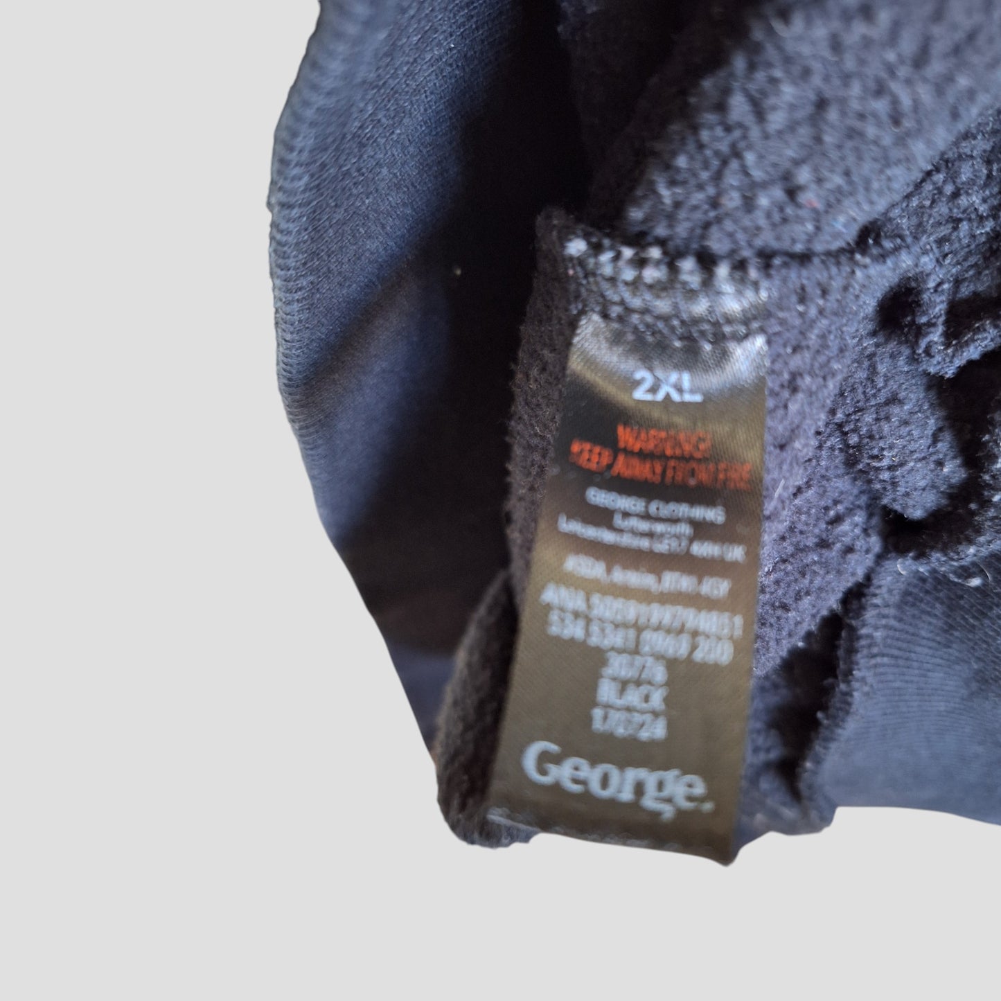 Close-up of a black "George" label inside an upcycled 2XL Fleetwood Mac nursing & pumping sweatshirt, showing washing instructions and a red safety warning; part of George's stylish eco-friendly maternity collection.