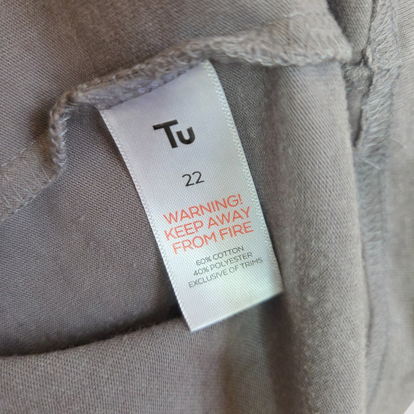 A close-up reveals the Tu label on an upcycled UK22 grey/pastel Bowie Band nursing t-shirt, with a red fire warning and material details (60% cotton, 40% polyester)—affordable fashion exclusive of trims.